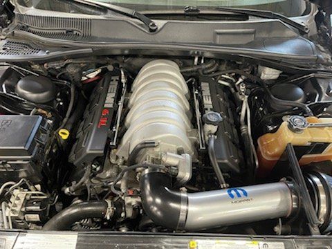 Engine bay of a black Dodge Challenger, displaying a silver intake and engine components.
