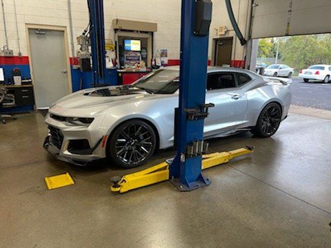 Silver Chevrolet Camaro on a lift in a repair shop.