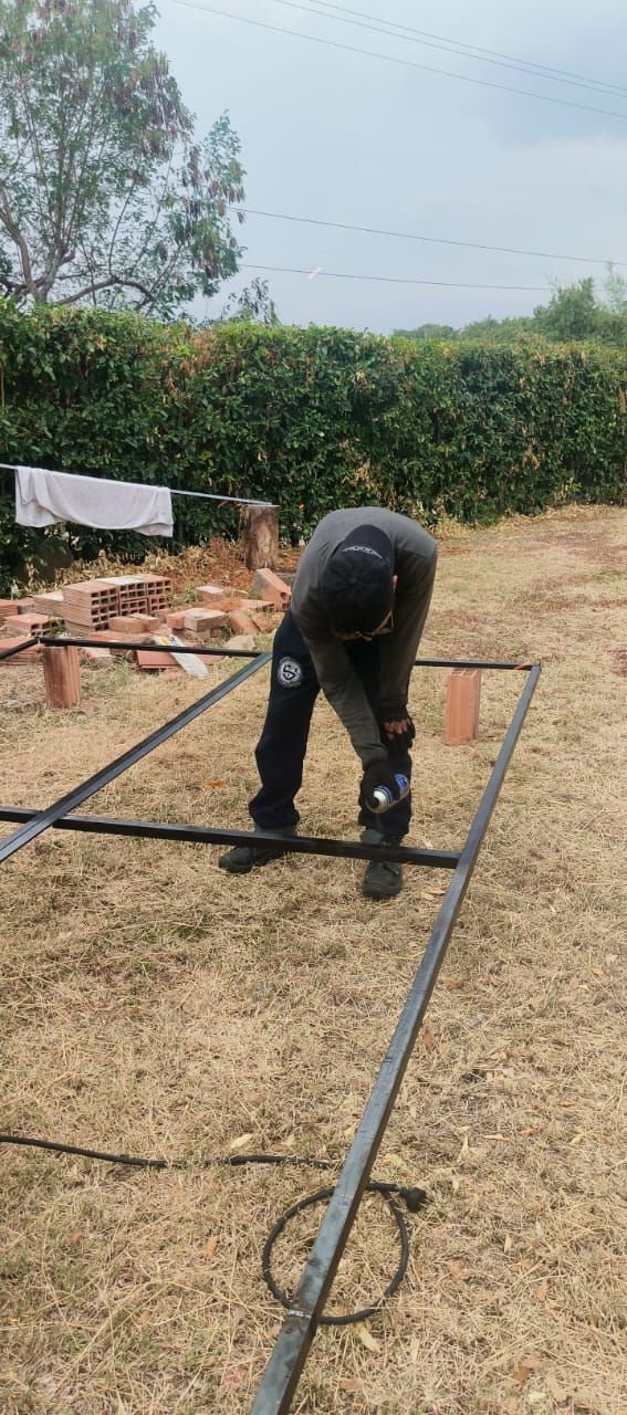 Persona agachada trabajando en una estructura metálica al aire libre en un campo seco.