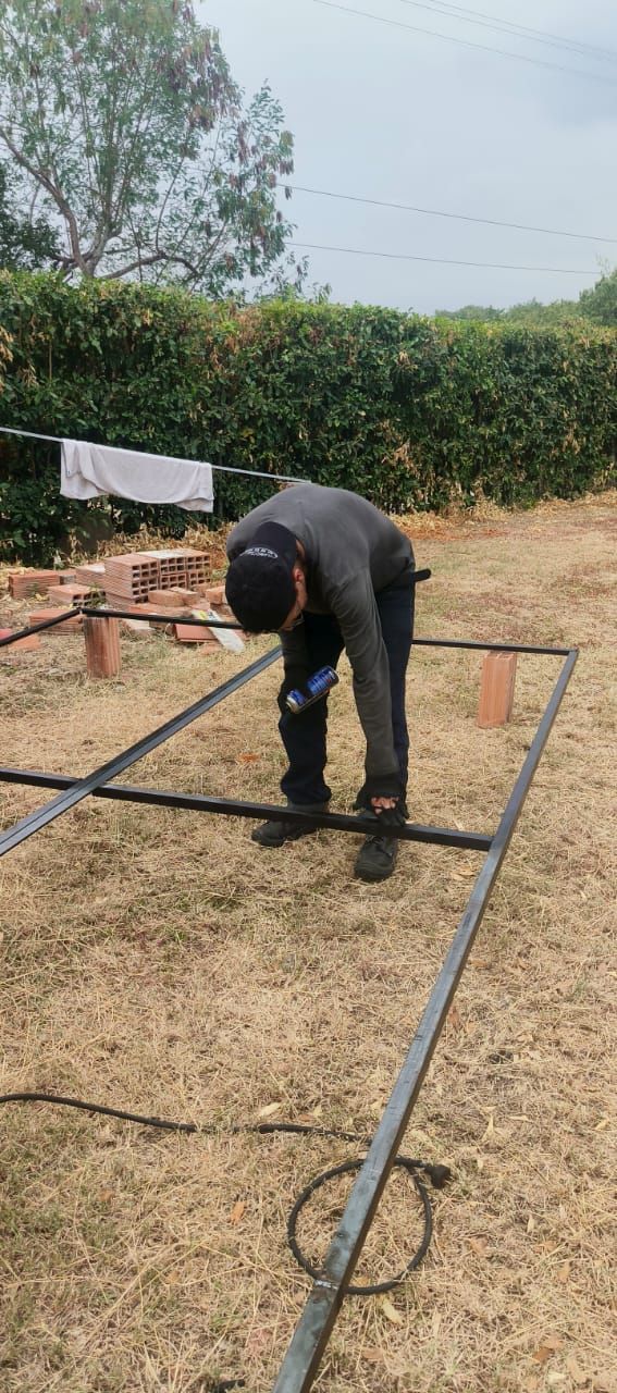 Persona inclinada sobre una estructura metálica al aire libre, trabajando en el suelo de un patio.
