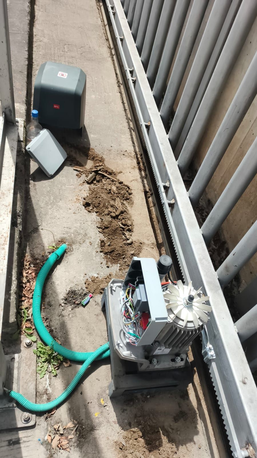 Área de servicio exterior con una manguera verde, equipo metálico y escombros junto a una cerca.