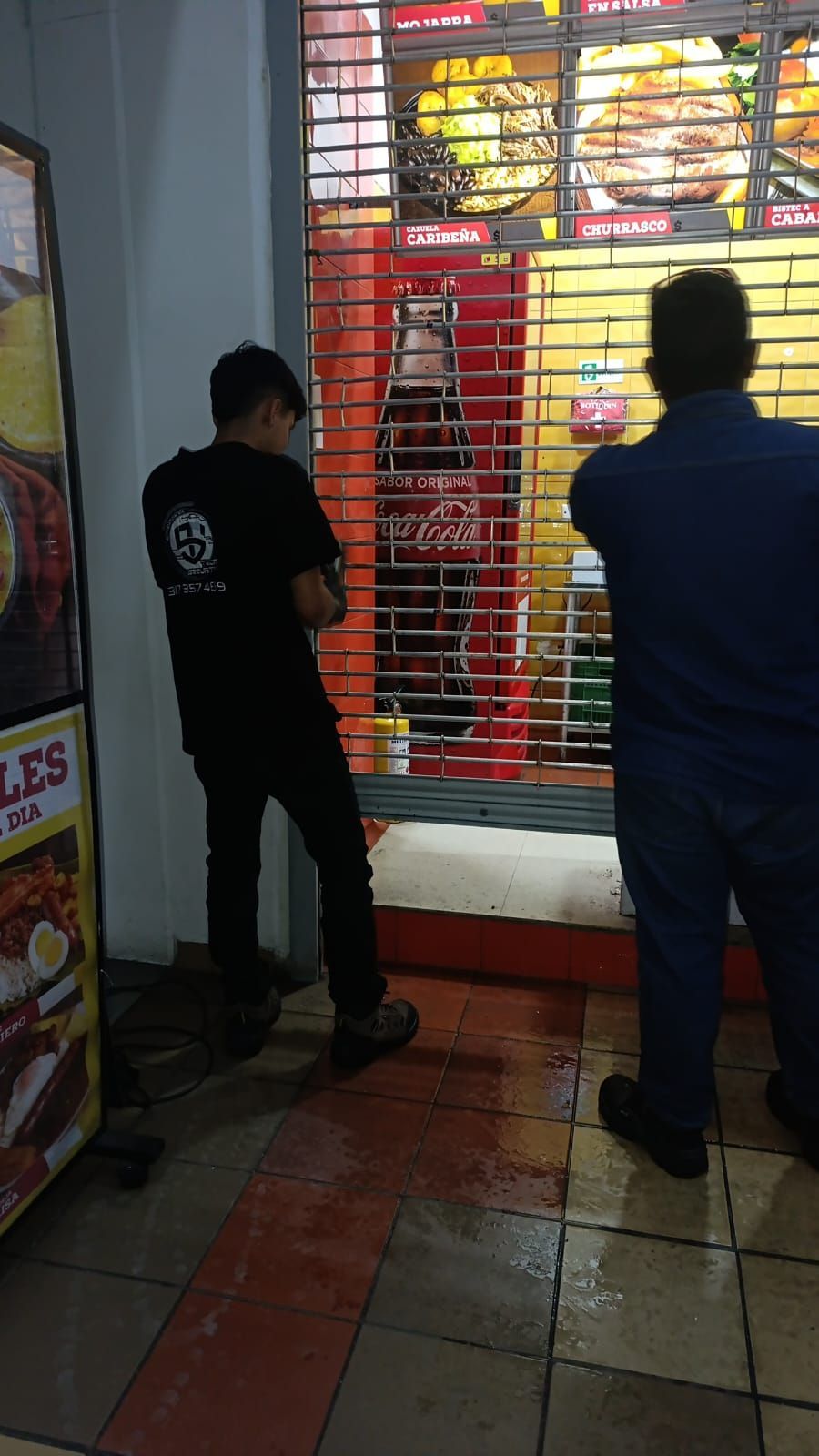 Dos personas de pie frente a una tienda cerrada con una puerta de seguridad