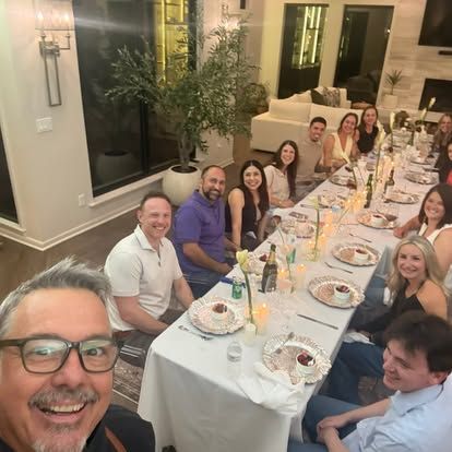 Friends gathered around a long dinner table, smiling in a warmly lit dining room.