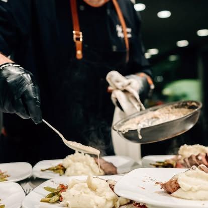 Chef plating creamy food onto white plates at a restaurant buffet