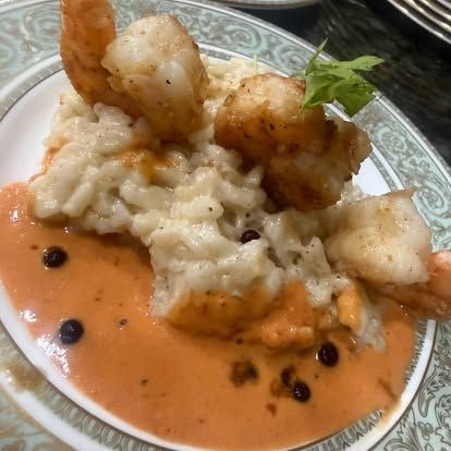 Plate of creamy risotto topped with seared shrimp, in a pink sauce with black peppercorns and parsley.