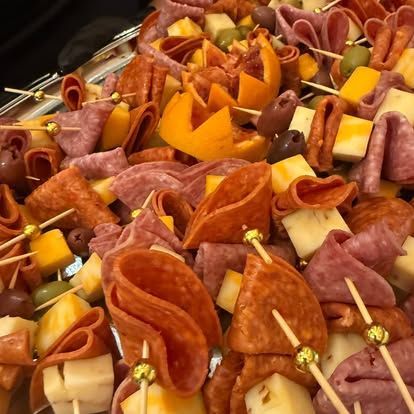 Assorted cured meats and cheese cubes arranged on toothpicks with orange fruit wedges on a platter