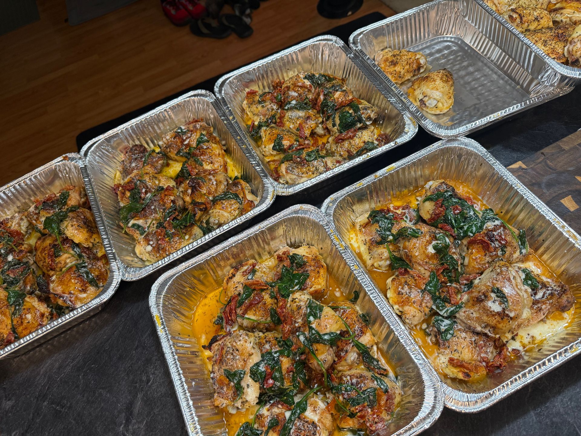 Foil trays of baked food topped with herbs, arranged on a table.