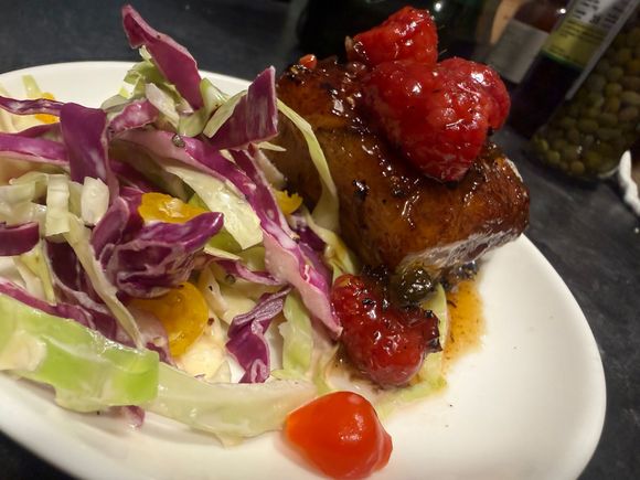 Plated steak with red sauce beside a shredded cabbage salad and cherry tomatoes