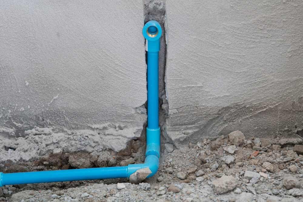 A Blue PVC Pipe is Being Installed in a Hole in a Wall — Rock Plumbing & Gasfitting In Airlie Beach, QLD