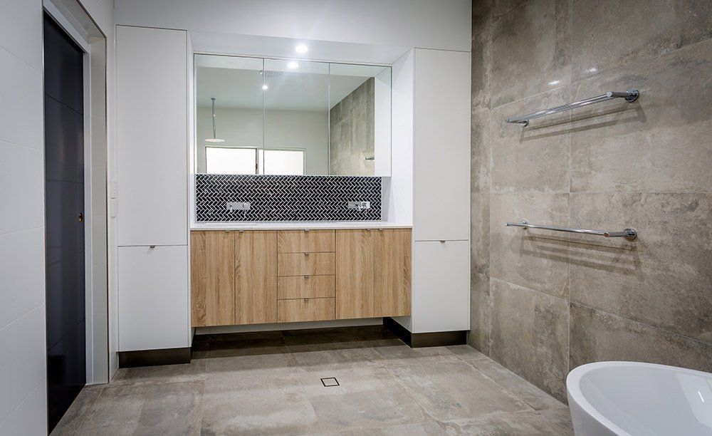 A Bathroom With a Tub , Sink , Mirror and Cabinets — Rock Plumbing & Gasfitting In Cannonvale, QLD