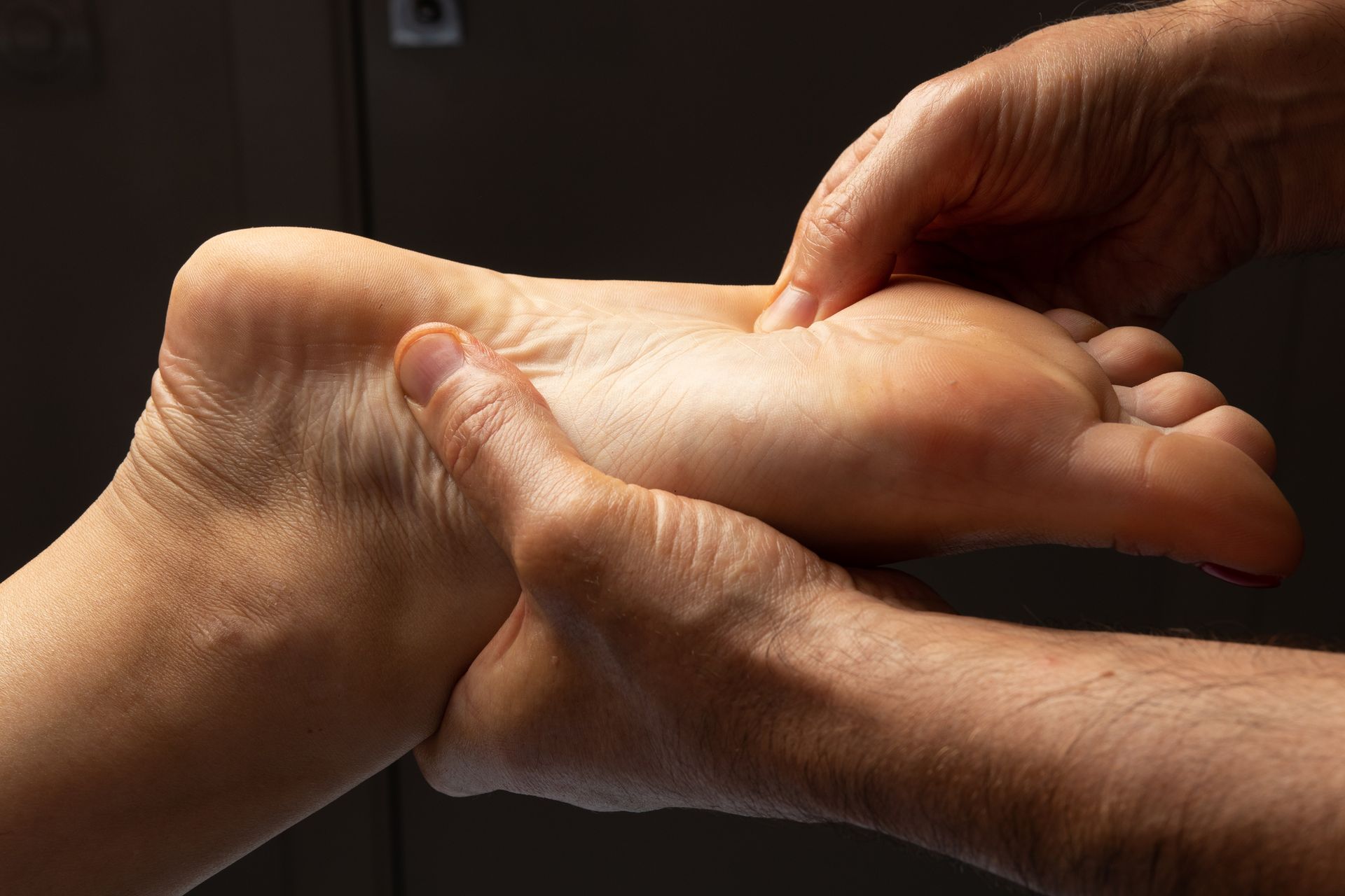 Close-up of a masseur’s hands as they press the mid-arch of a foot with their thumb.