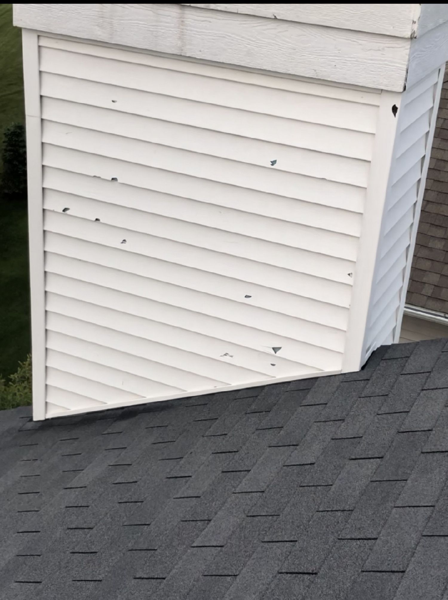 White vinyl-sided house corner above dark gray shingled roof.