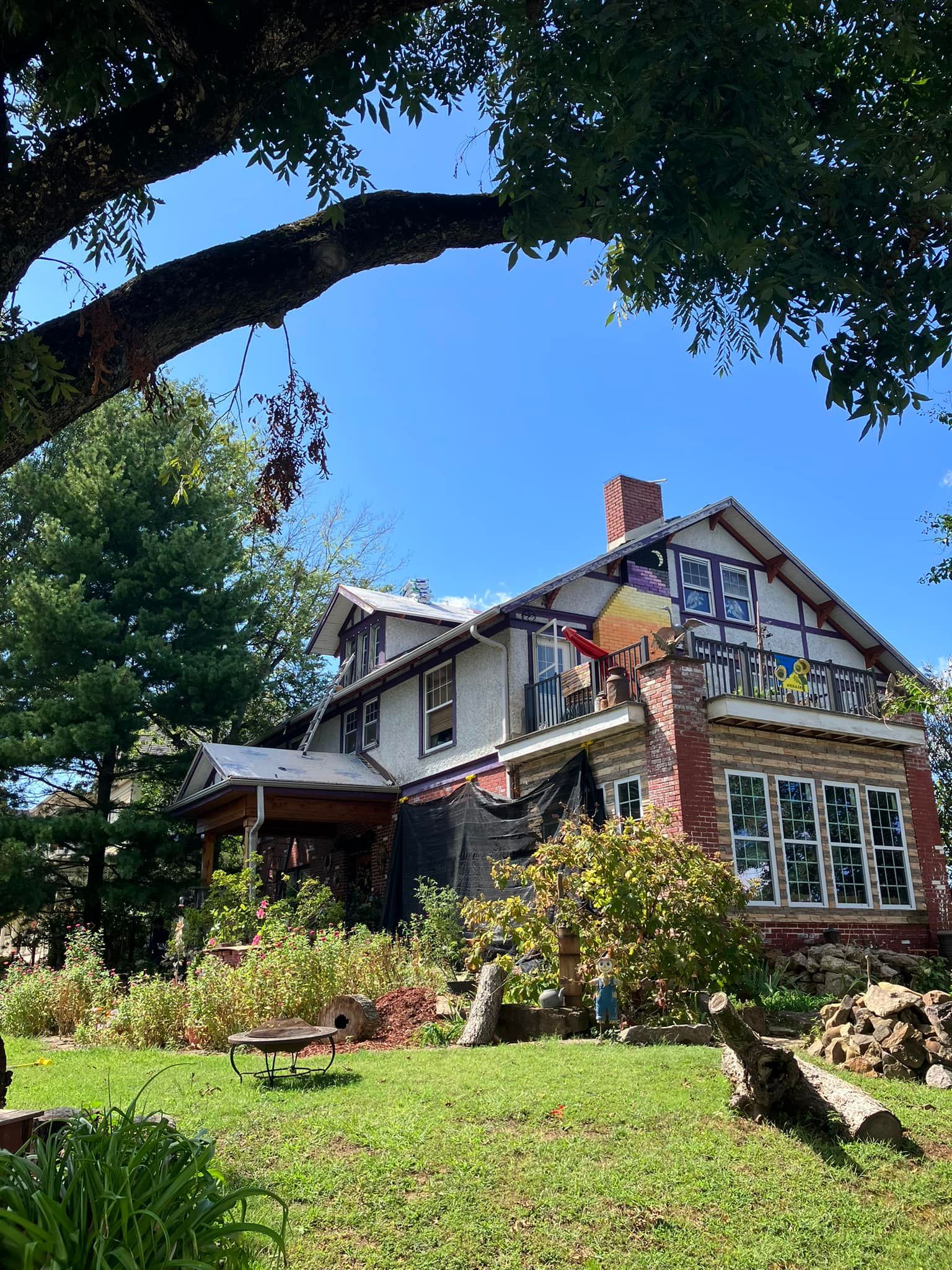Quaint house with a steep roof and garden, framed by large tree branches under a blue sky