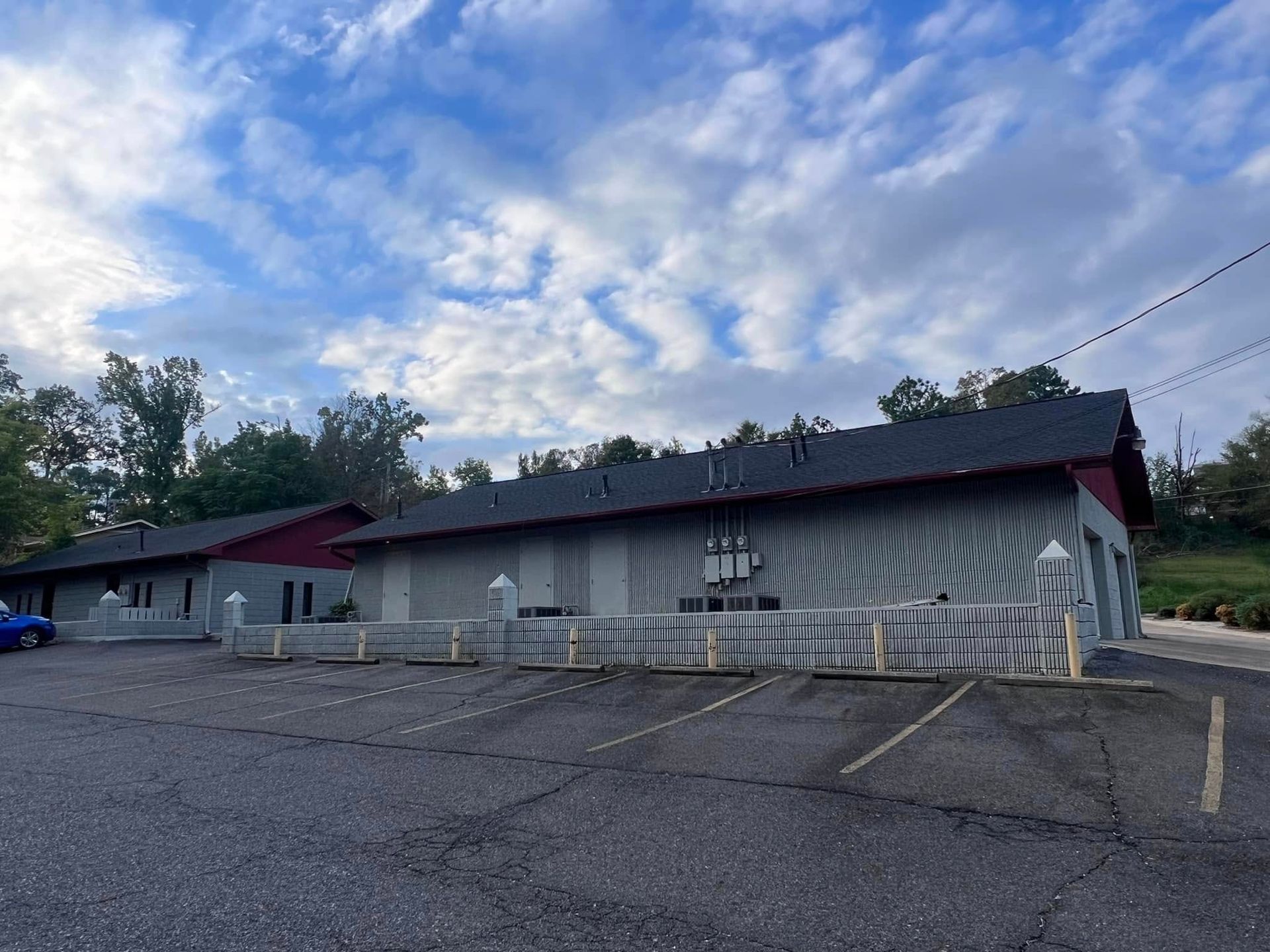 Low building with gray awning and white fence in an empty parking lot under a cloudy sky