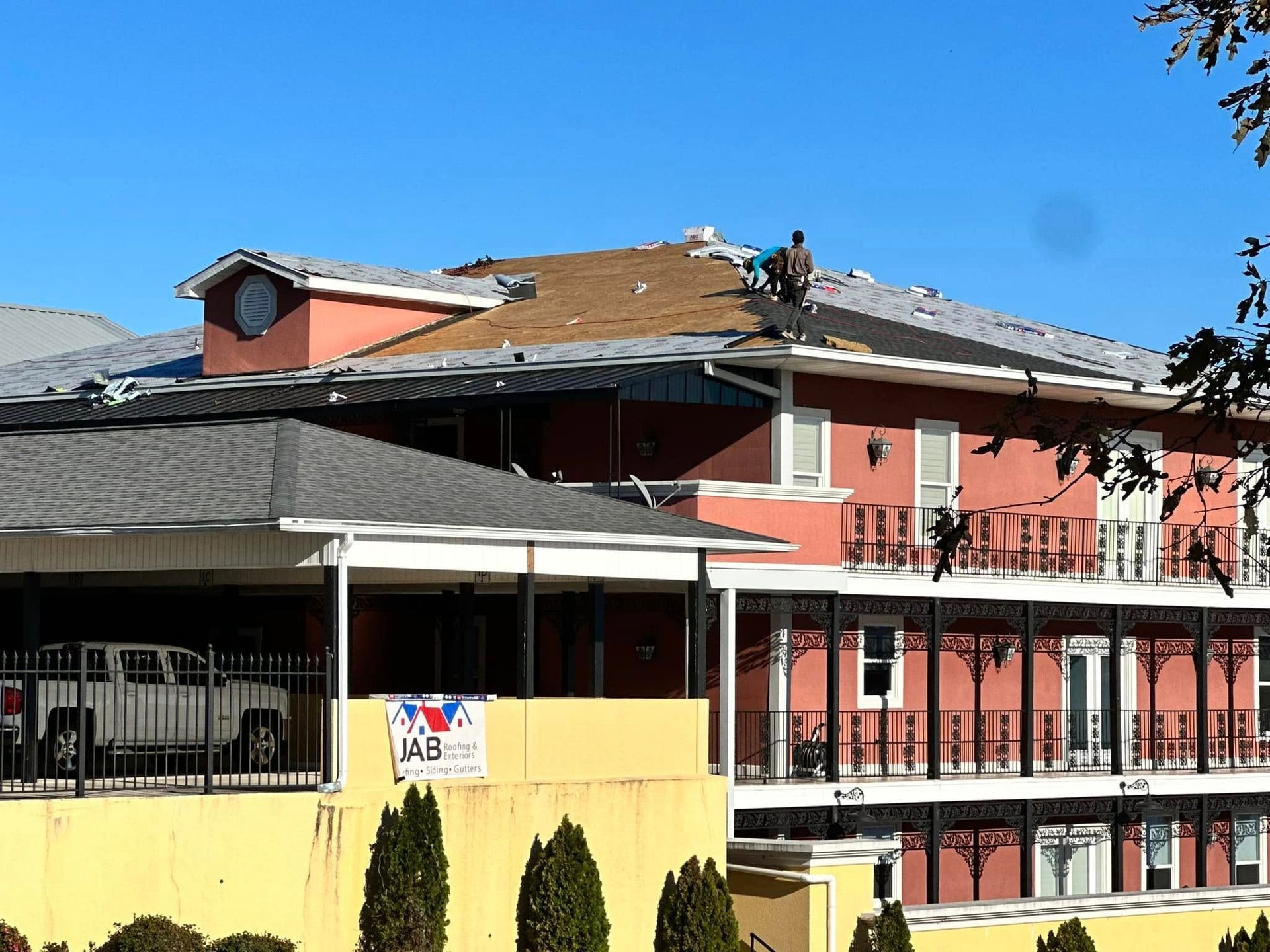 A red and yellow apartment building with balconies under a blue sky, with workers on the roof.