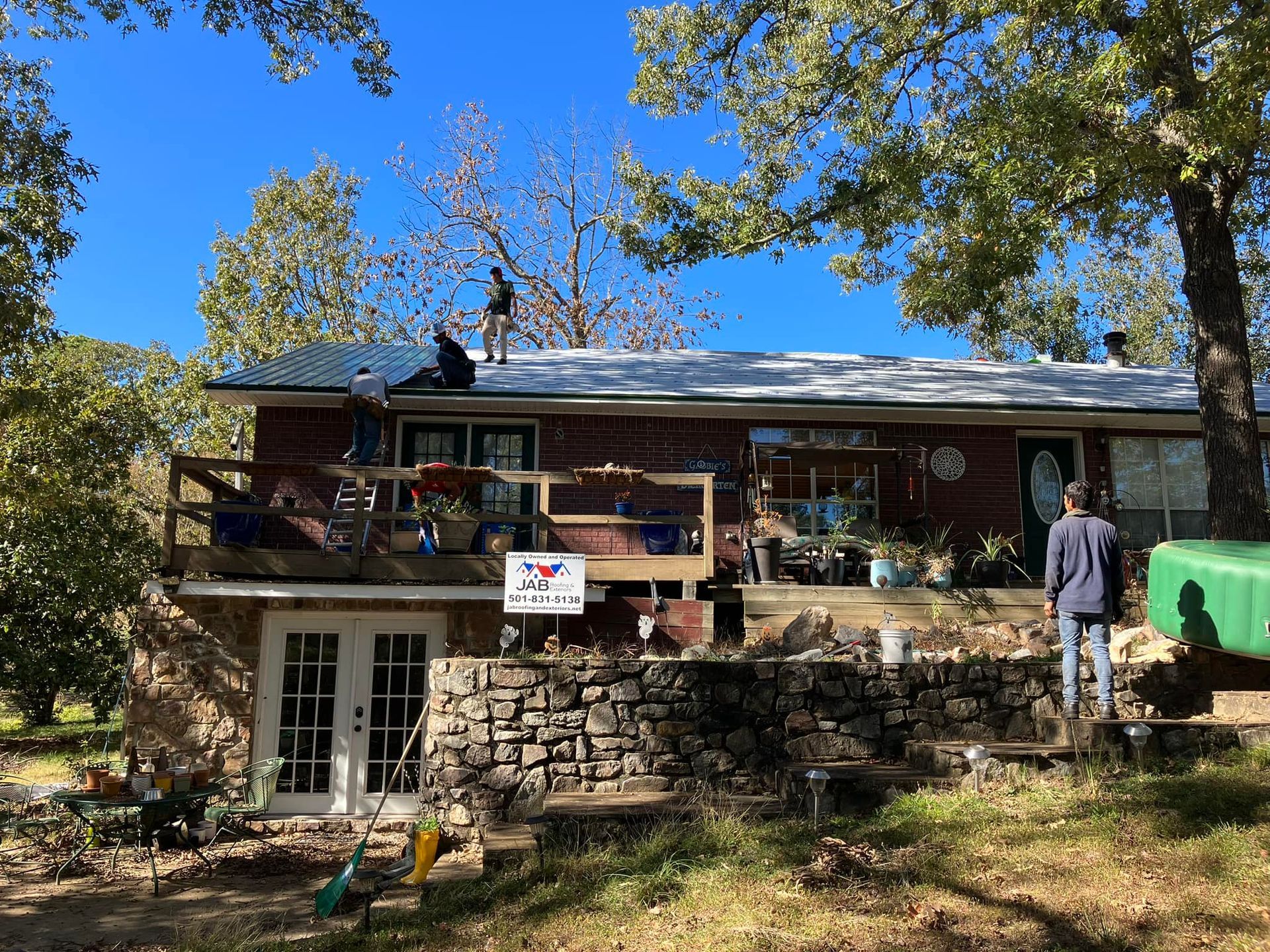 Stone house with balcony, trees, and a person standing outside on a sunny day