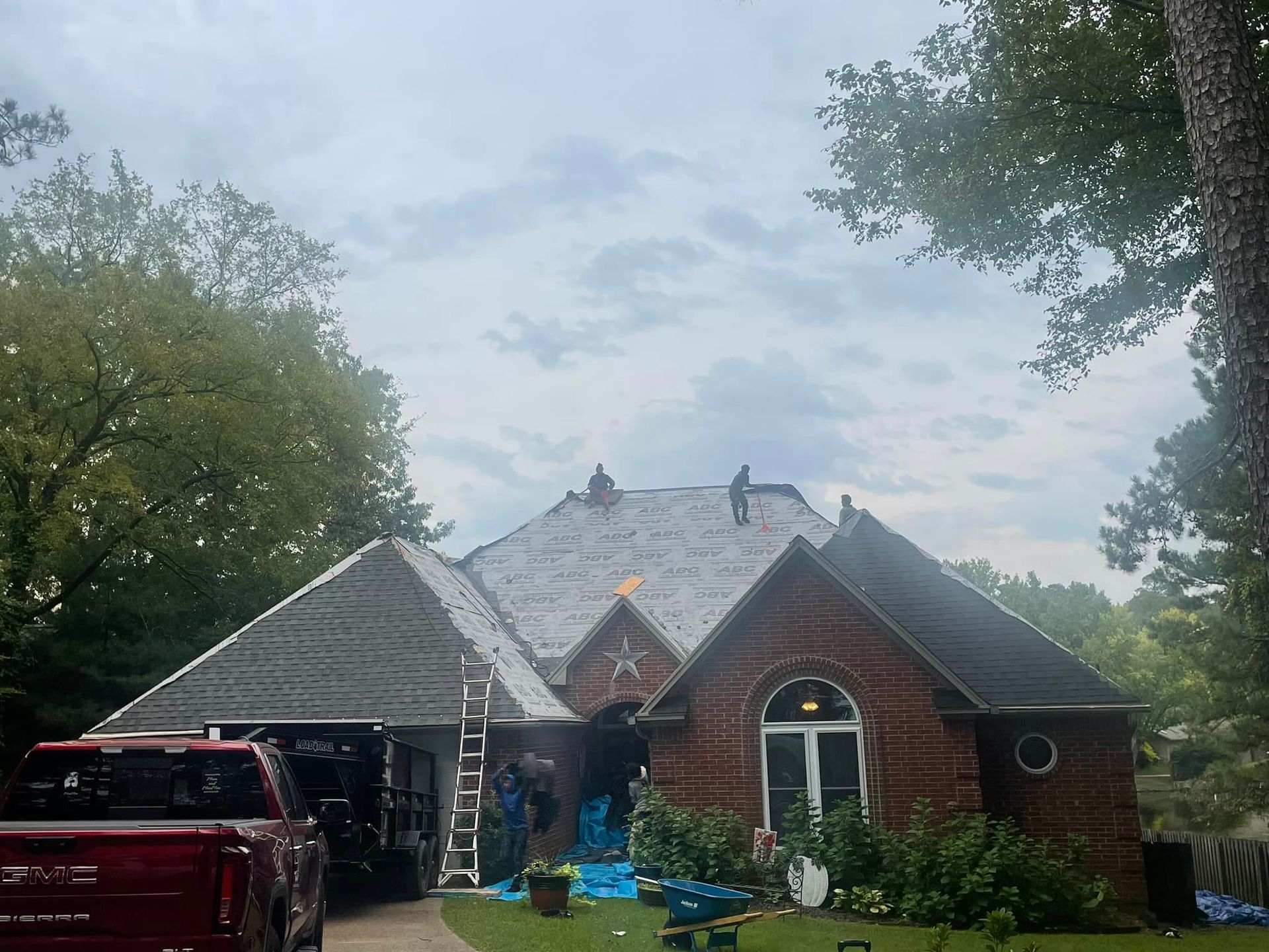 Red brick house with gray roof, red truck in driveway, surrounded by trees under a cloudy sky