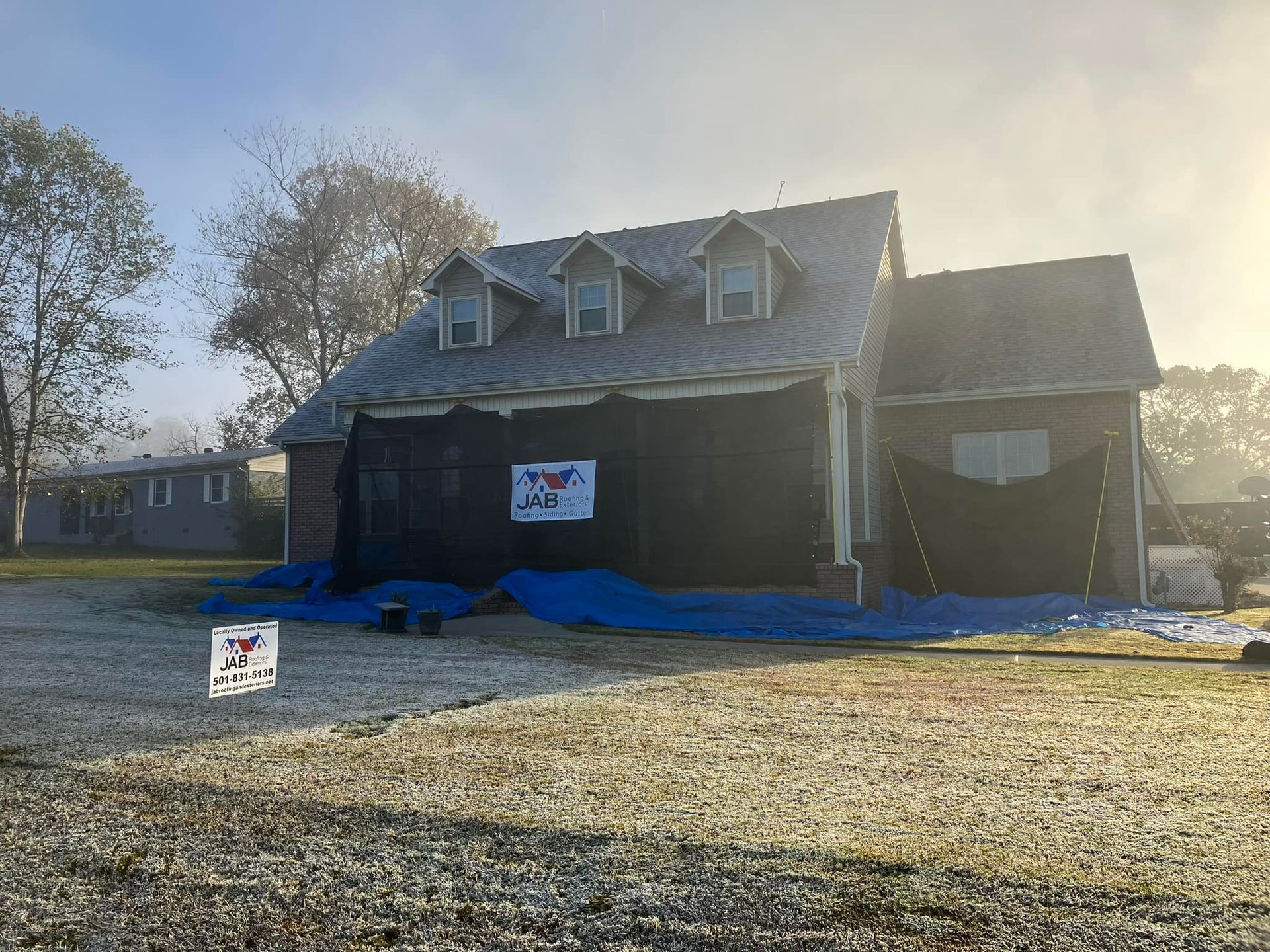 House under construction with dark exterior wrap, blue tarp on ground, and signs in the yard.
