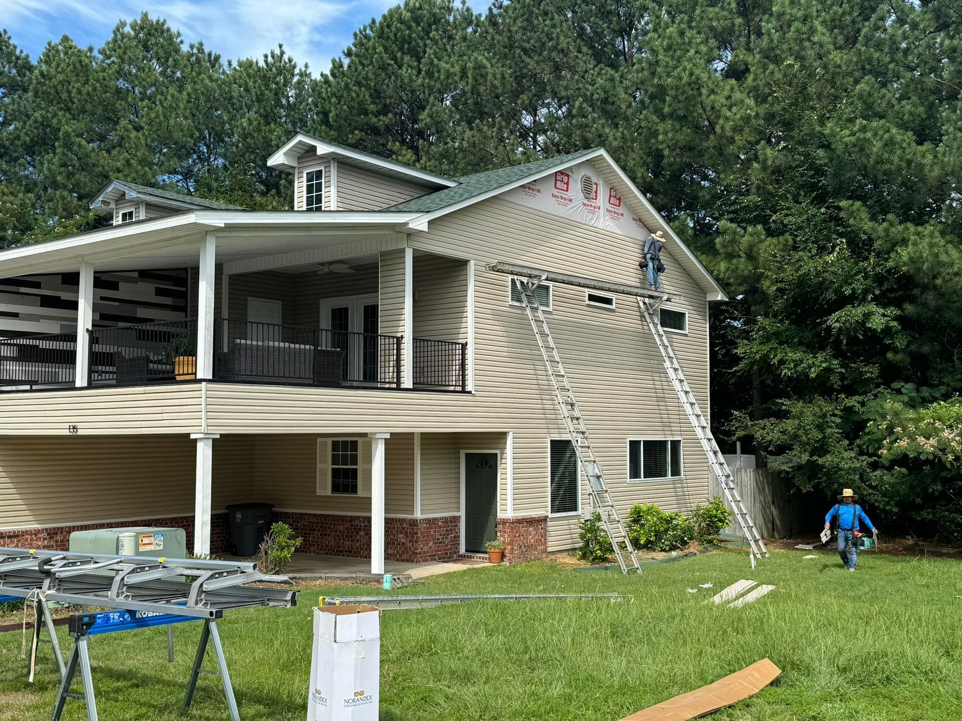 Two-story house with damaged siding and a ladder, with a worker on the lawn.