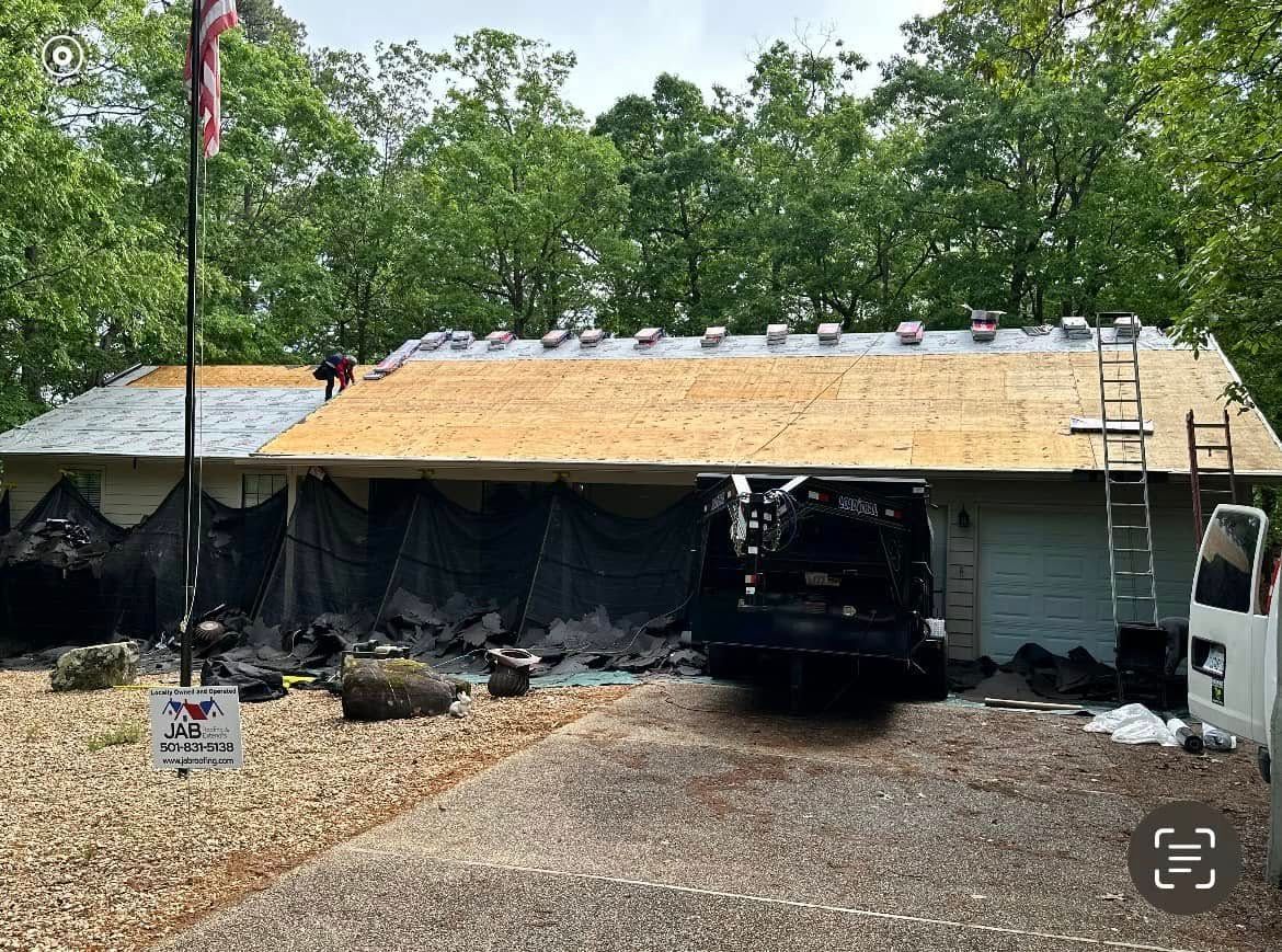 Large carport with a tan roof tarp over a dark SUV, damaged siding, and a ladder beside a gravel driveway.