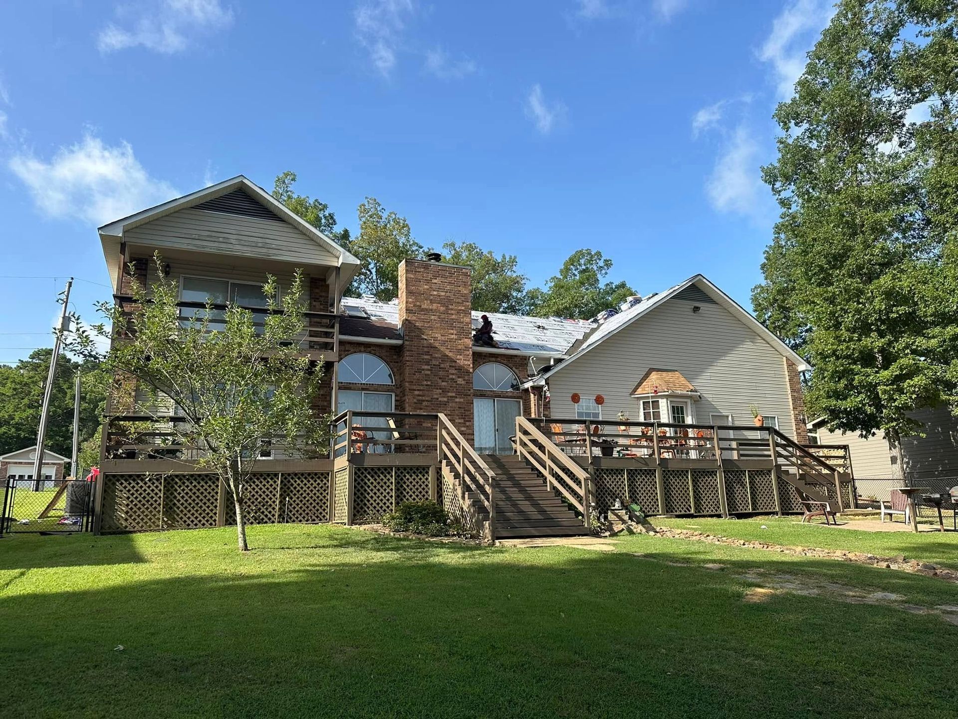 Two-story house with wooden deck, central brick chimney, and green lawn under a blue sky