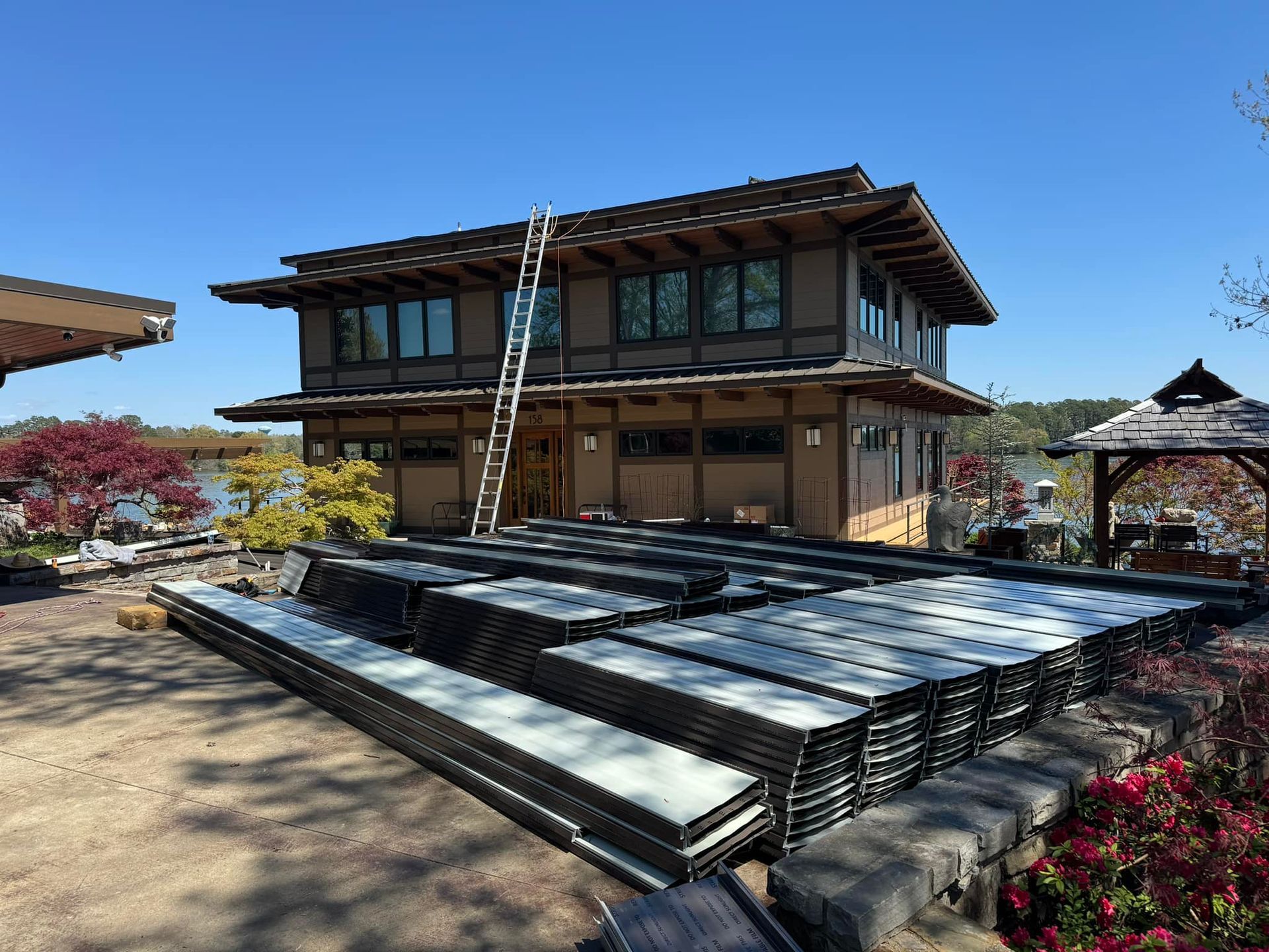Two-story house under construction with ladders, stacked materials, and flowerbeds in front