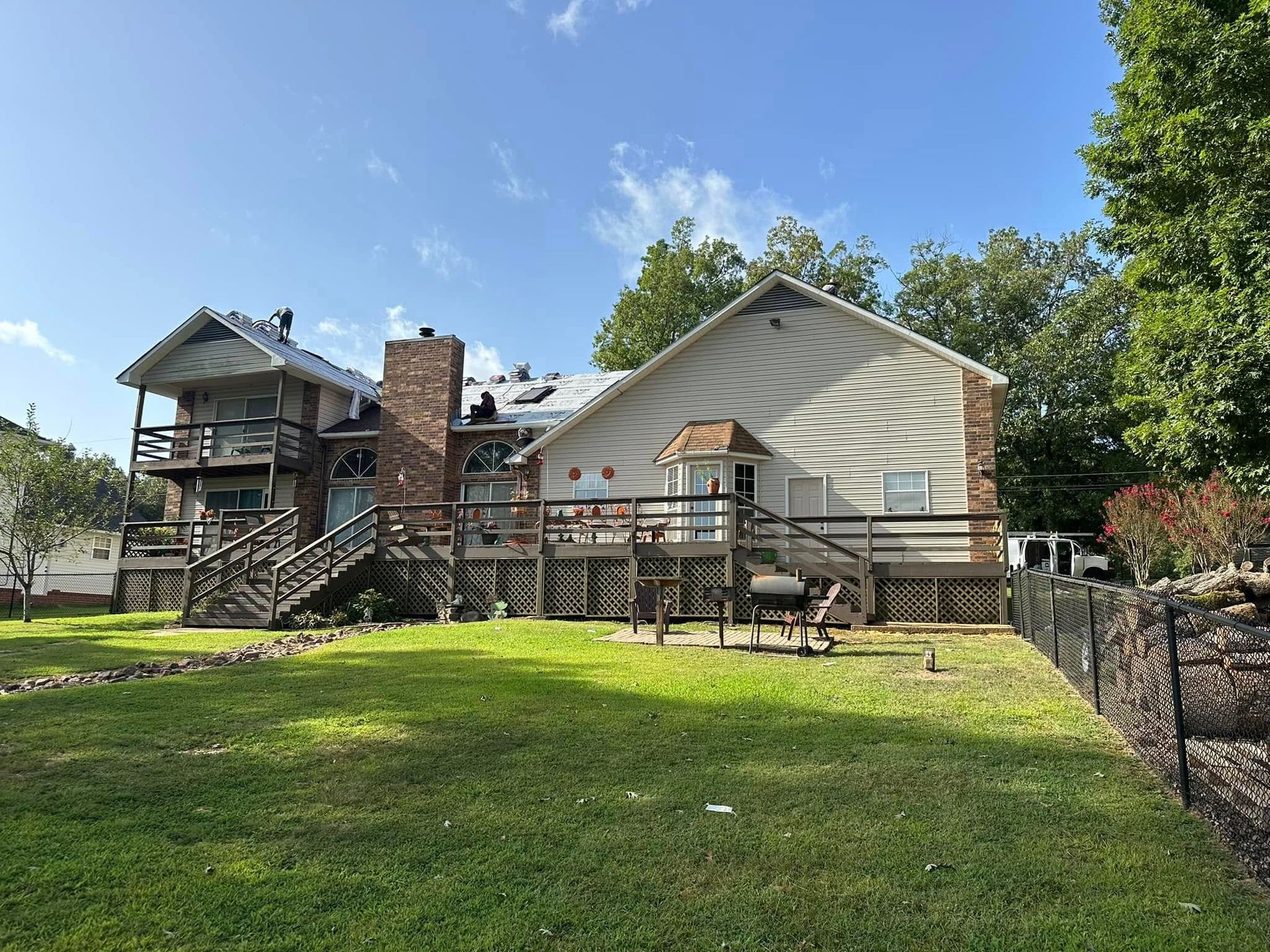 House with wooden deck and stone chimney on a sunny green lawn under a blue sky