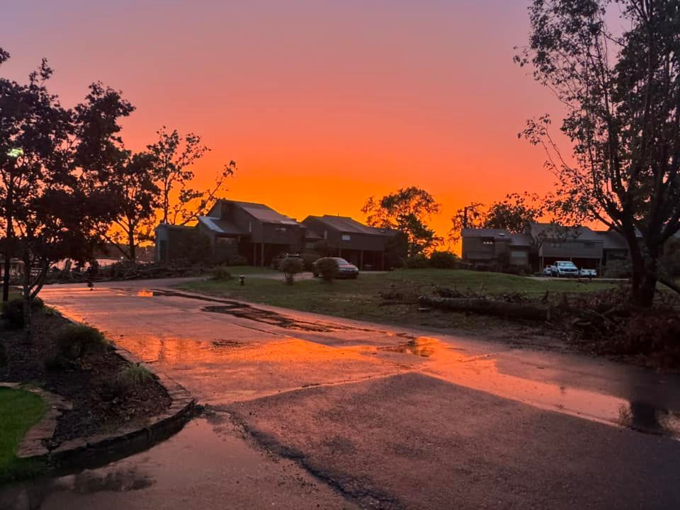 Sunset over wet suburban street with glowing orange sky and silhouetted trees and houses