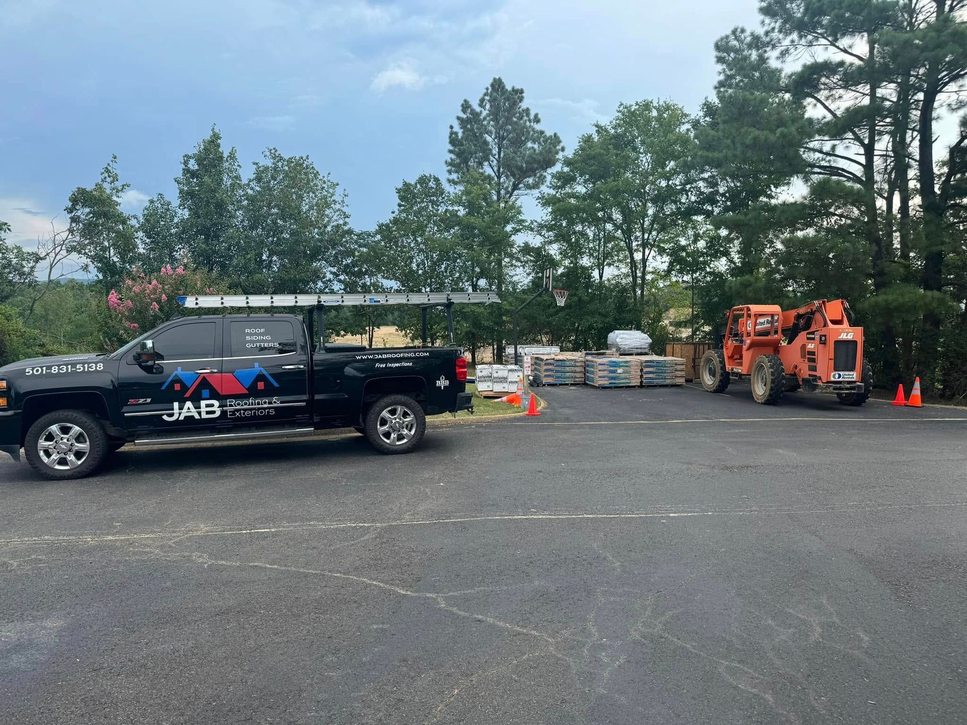 Parking lot with black utility truck, orange lift equipment, cones, and trees in the background