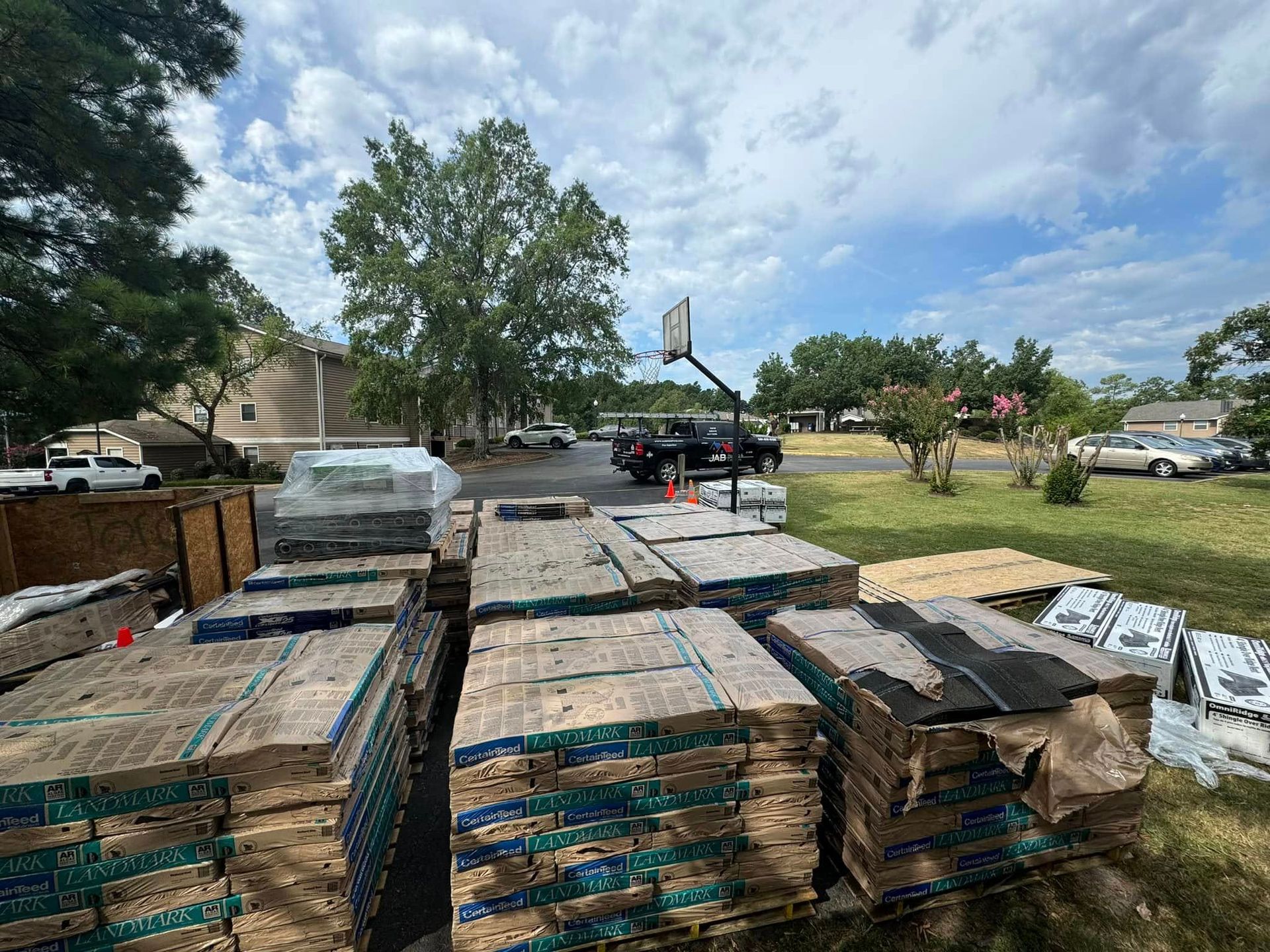 Stacks of wrapped pallets in a yard with a truck and trees under a partly cloudy sky