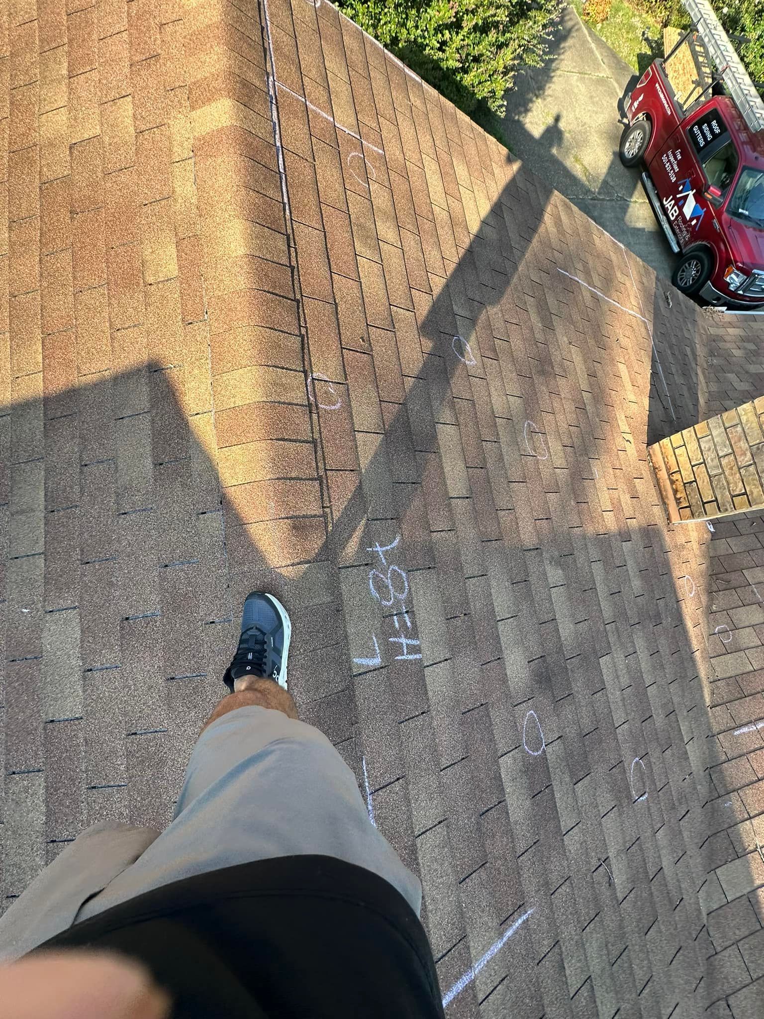 Looking down from a rooftop at a person’s foot, brick roof shingles, and a red truck below.