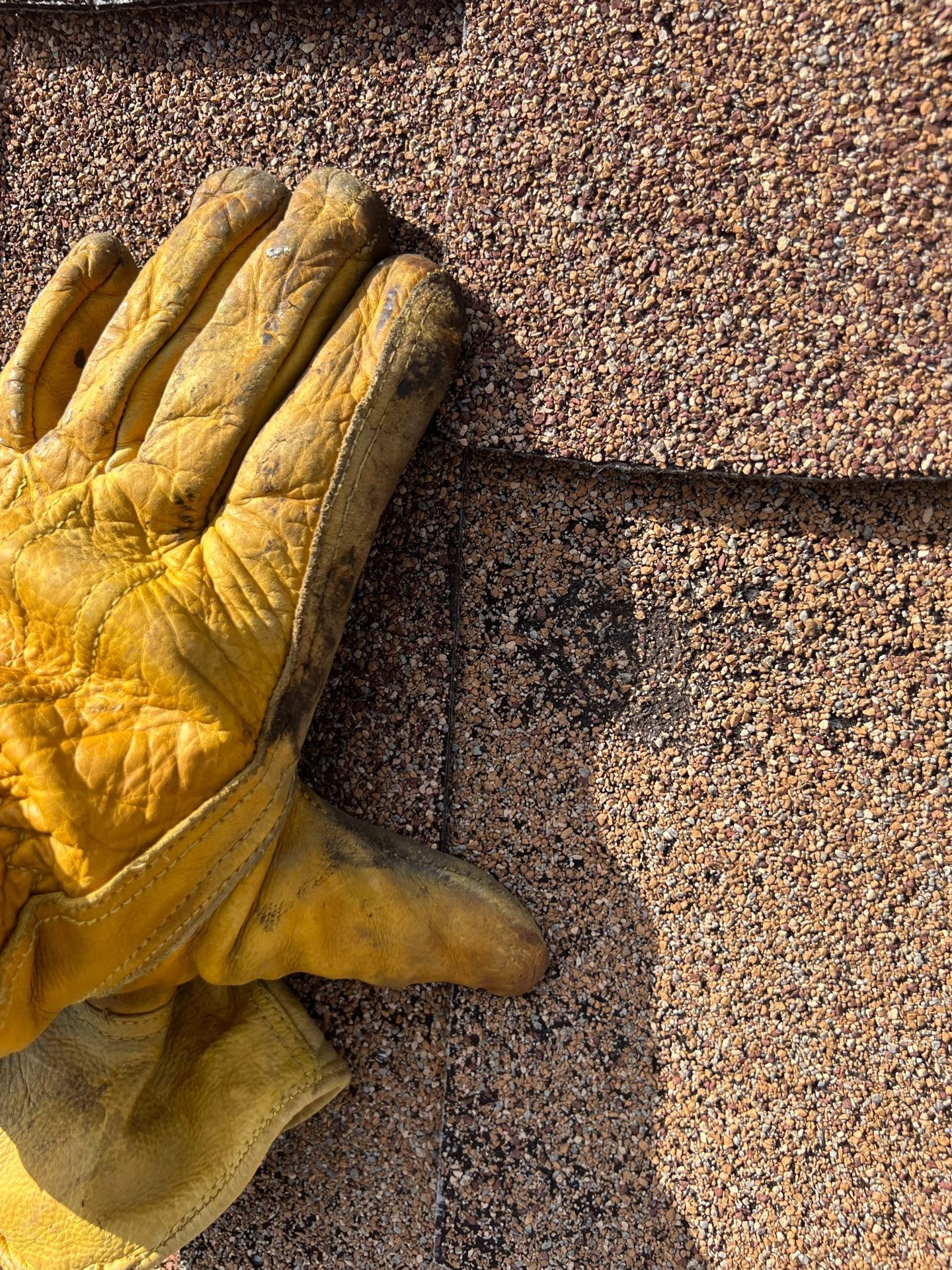 Yellow work glove on a rough brown surface, with one finger extended.