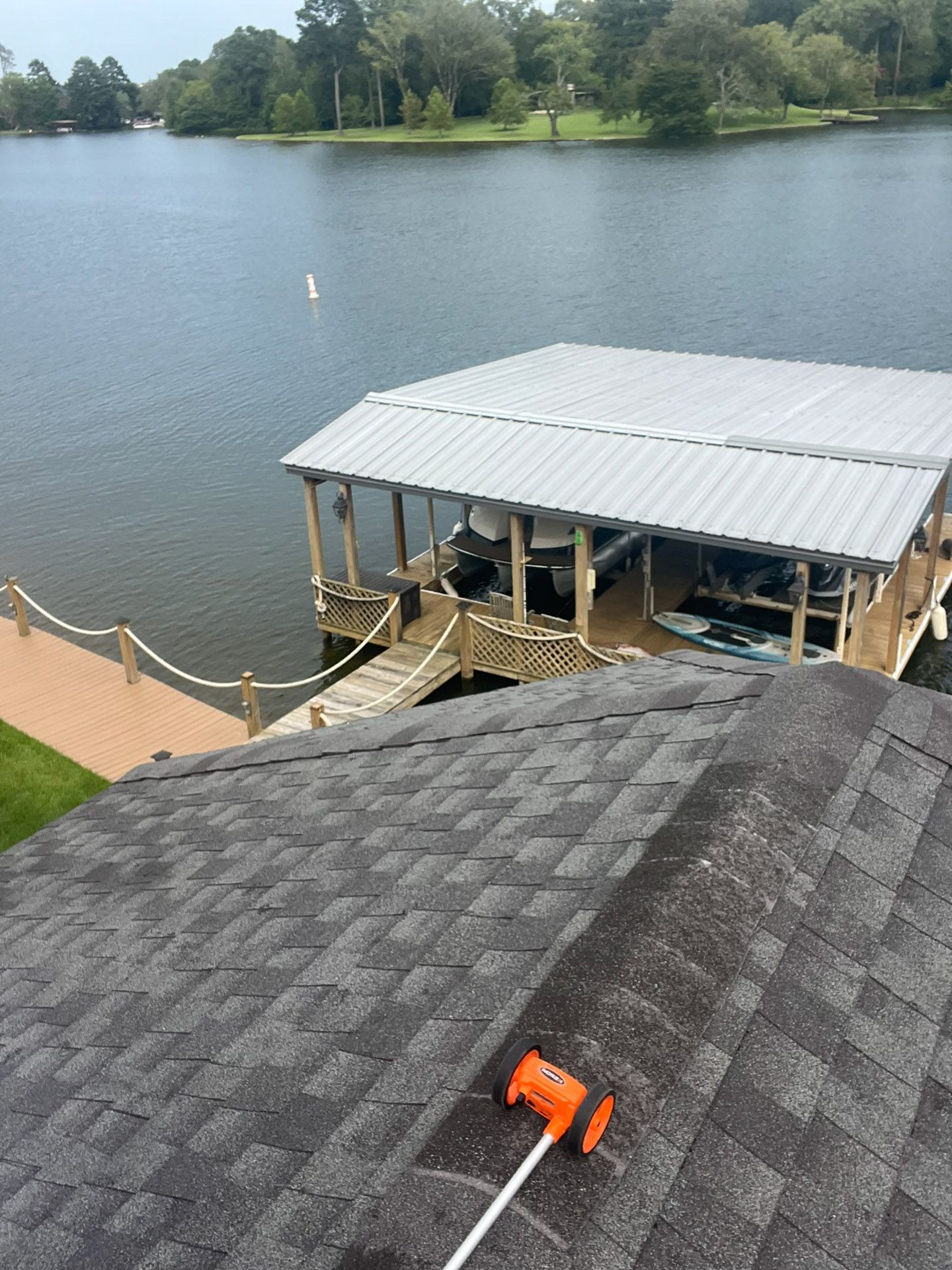 Lakefront dock and roof with an orange tool in the foreground, viewed over calm water.