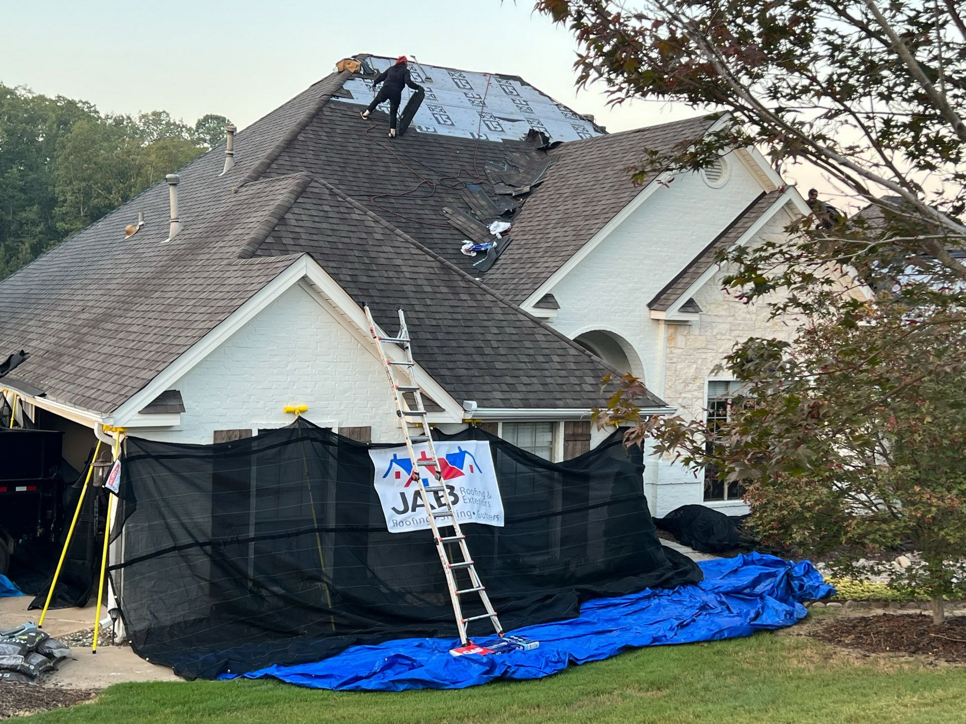 Workers repairing a roof with black tarps and a ladder on a suburban house