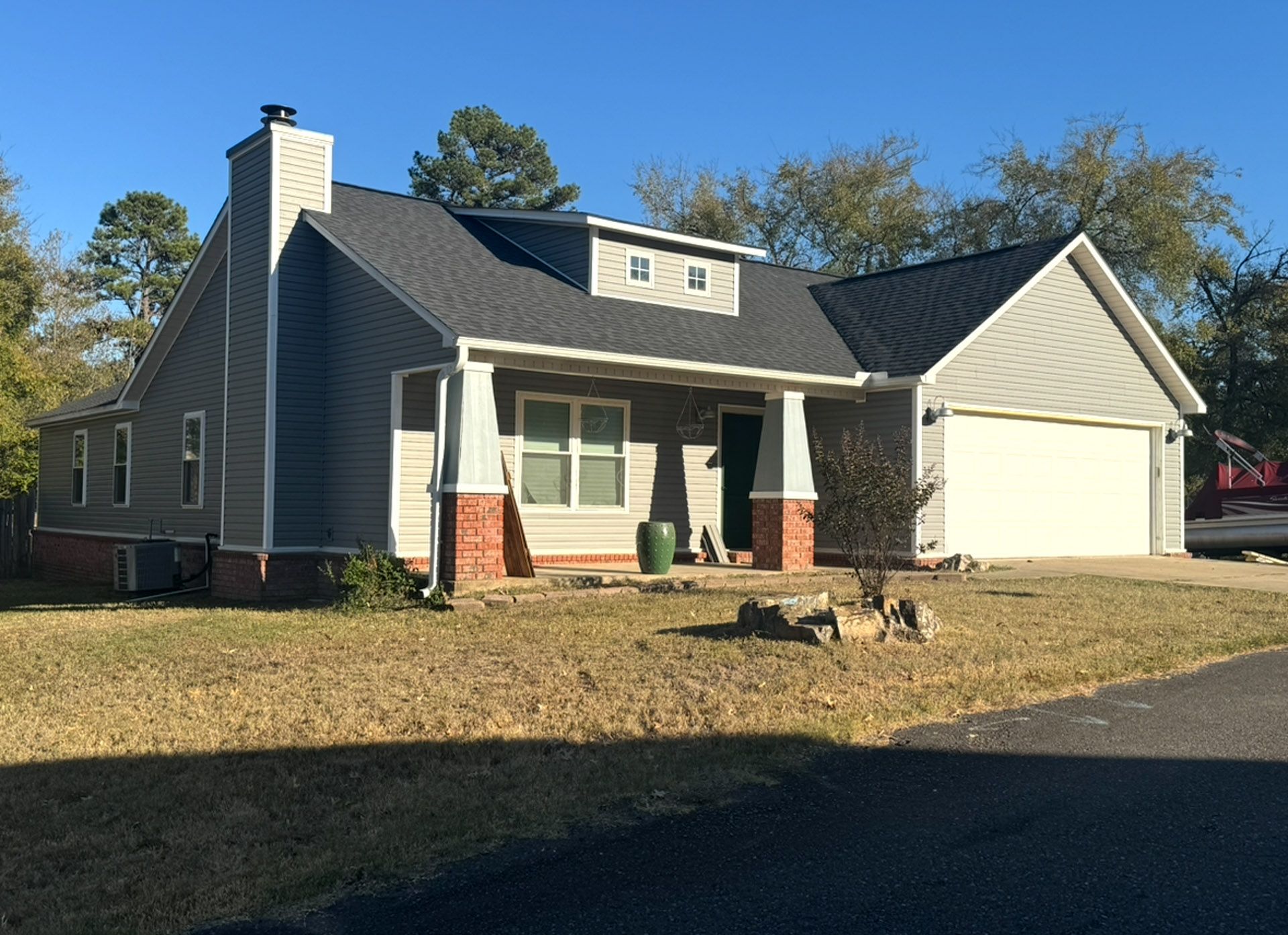 Suburban house with gray siding, white garage, and front porch in a sunny yard