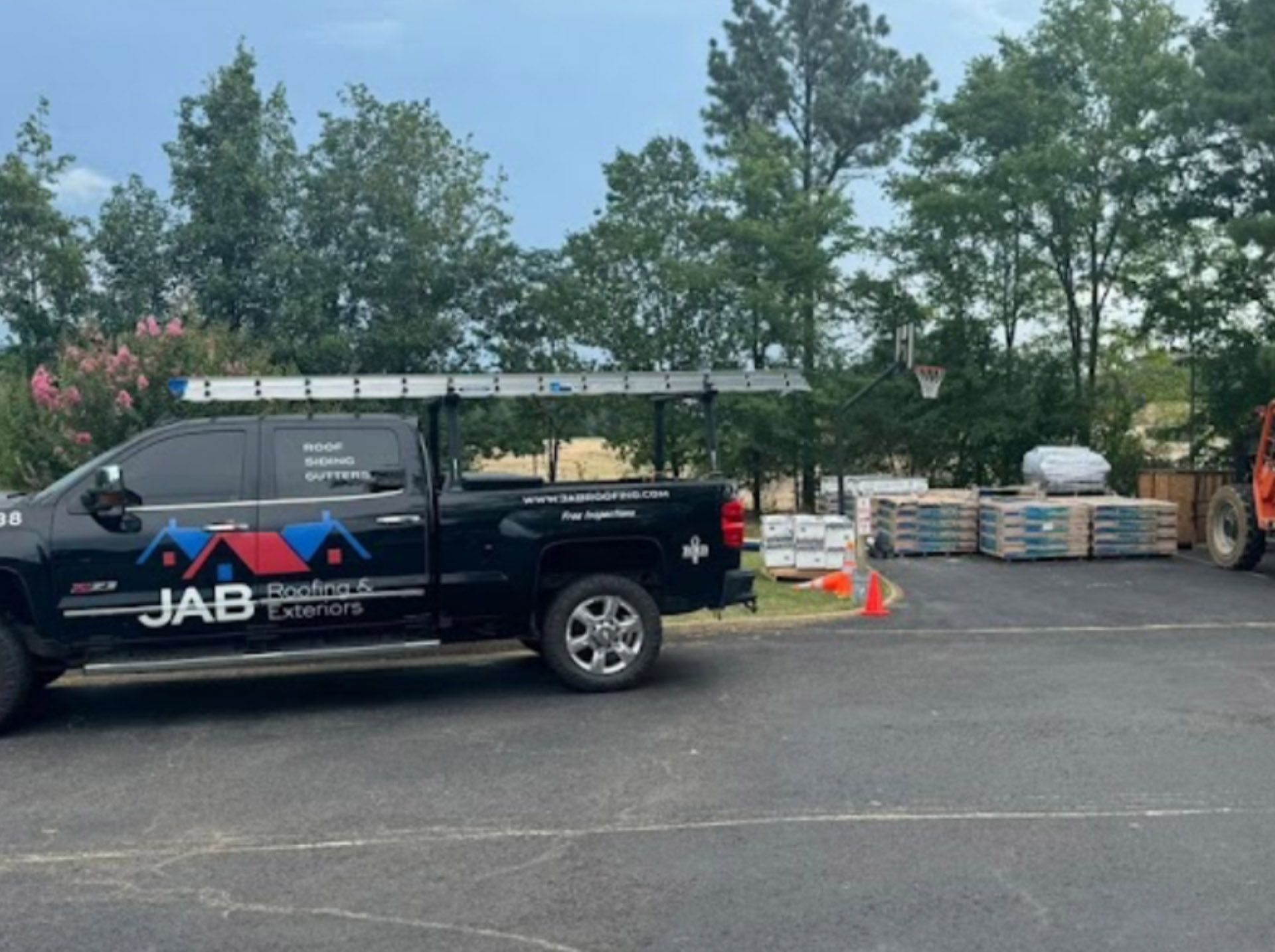 Black JAB service truck parked beside construction materials and cones in a lot with trees behind.