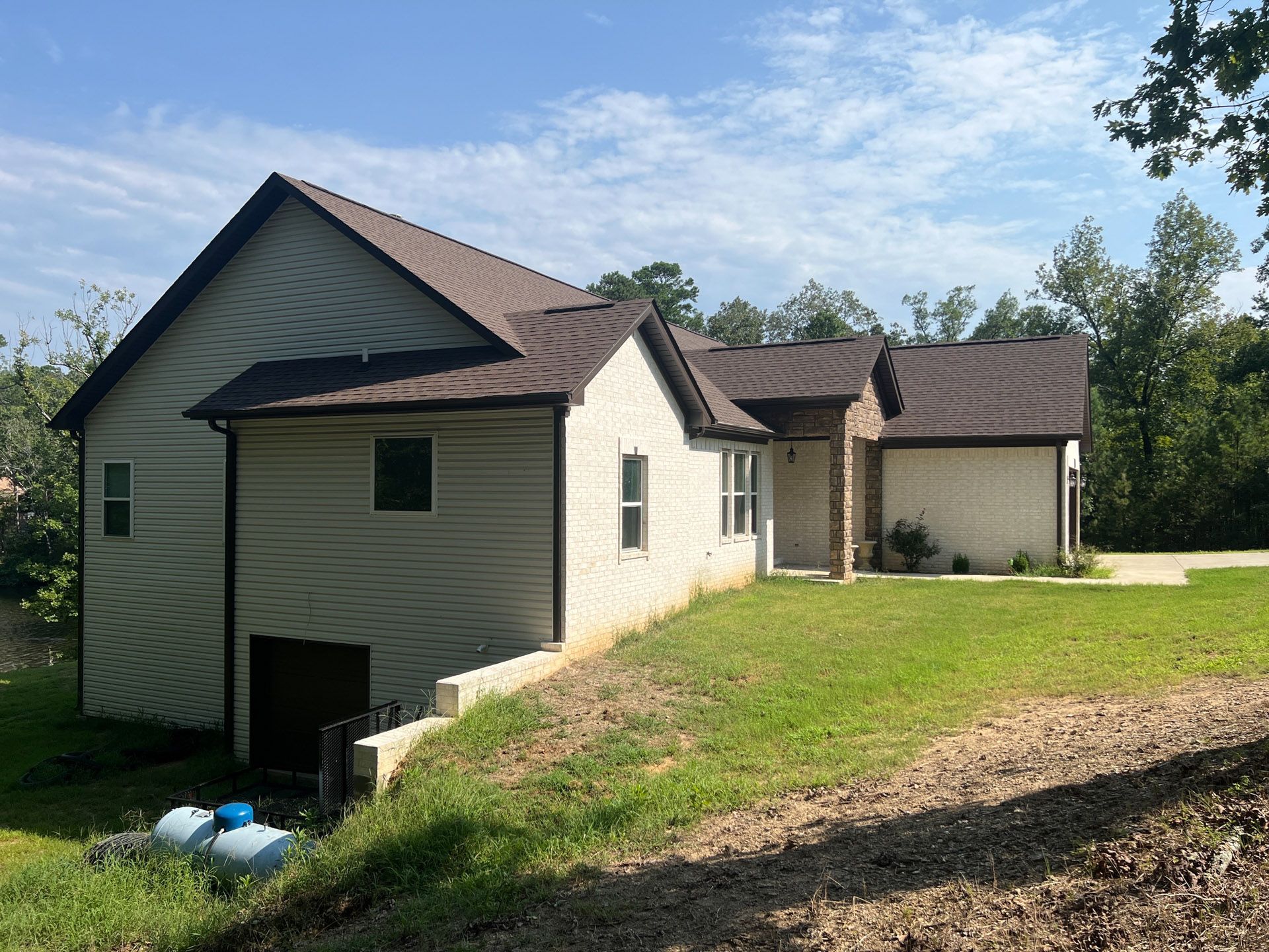 Single-story house with beige siding, brown roof, and attached garage on a grassy lot under a blue sky
