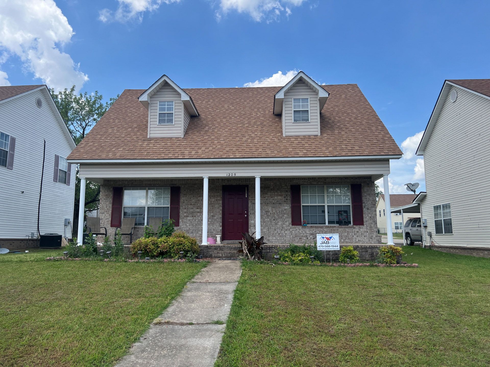 Small brick house with a red roof, front porch, and central walkway under a blue sky.