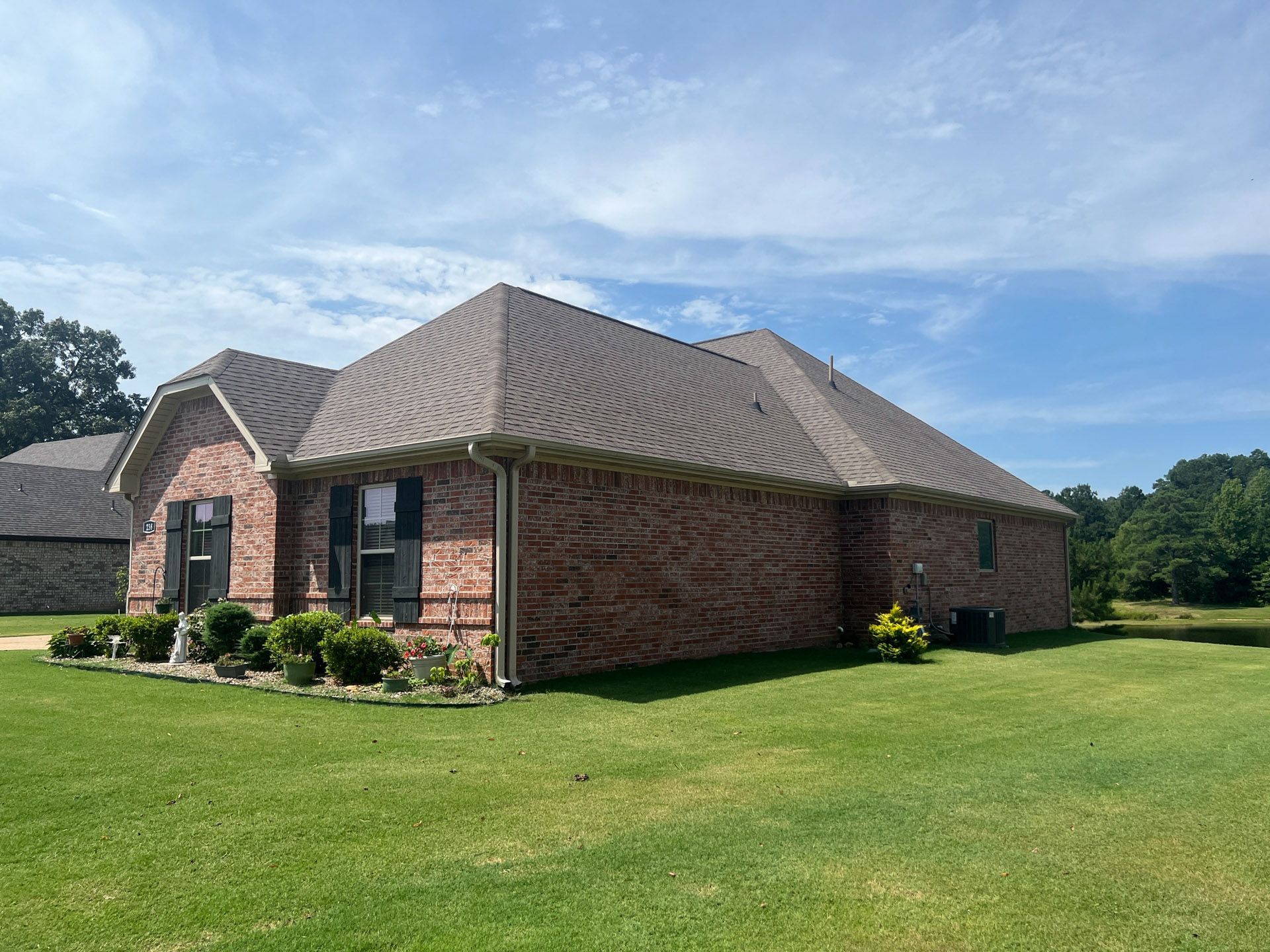 Brick house with tan roof on a green lawn under a blue sky