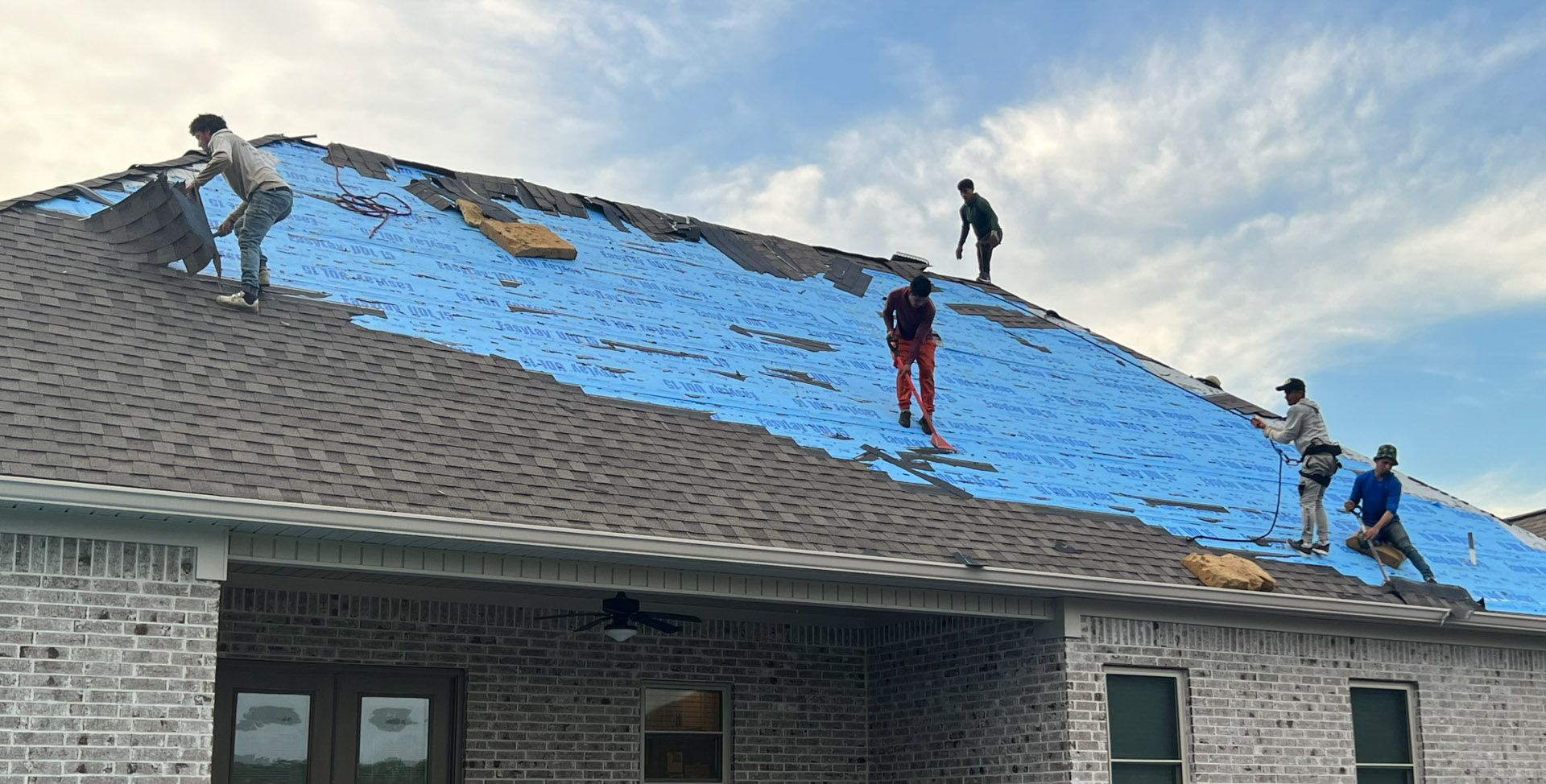 Workers covering a roof with blue tarps on a suburban house after storm damage
