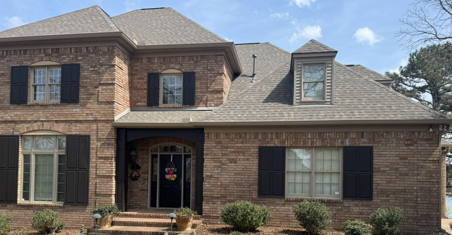 Two-story brick house with dark shutters, covered porch, and a dormer under a gray roof