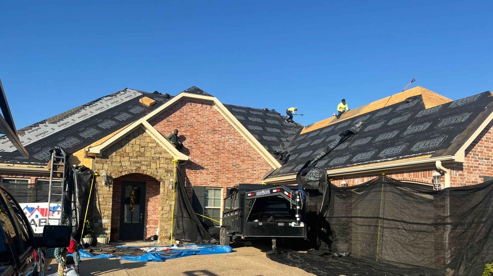 New homes under construction with brick facades, dark roofs, and workers on the roof under a clear blue sky