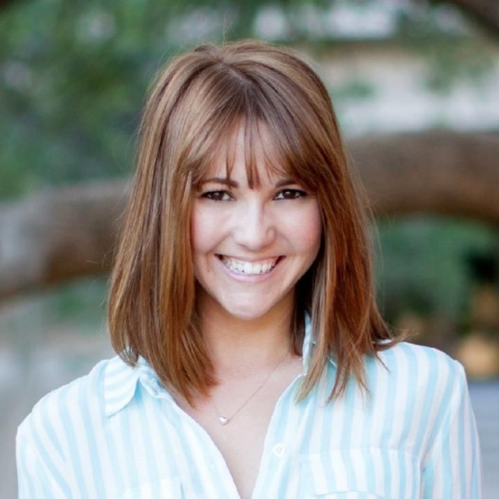 A woman with red hair is wearing a striped shirt and smiling.