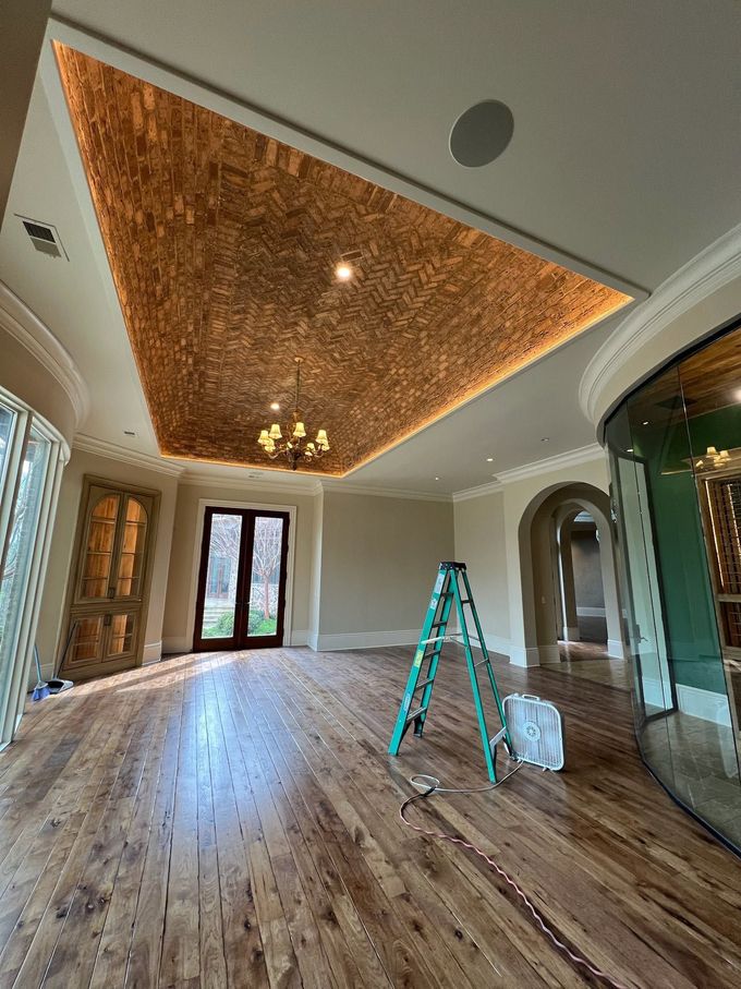 Spacious room with wood floors, ornate ceiling, and a ladder in the center under renovation.