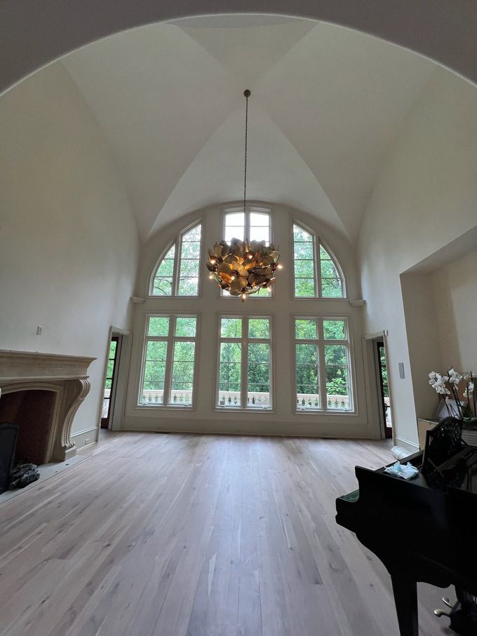 Bright vaulted room with large arched windows, chandelier, fireplace, and light wood floors