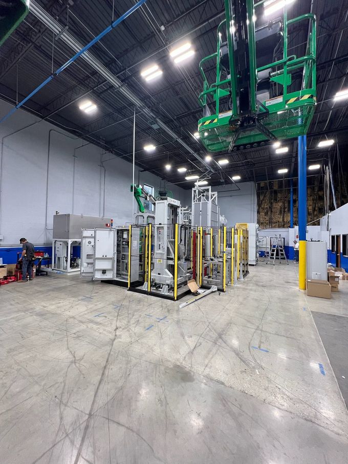 Warehouse interior with industrial equipment, tall green machinery, and rows of storage racks on a concrete floor