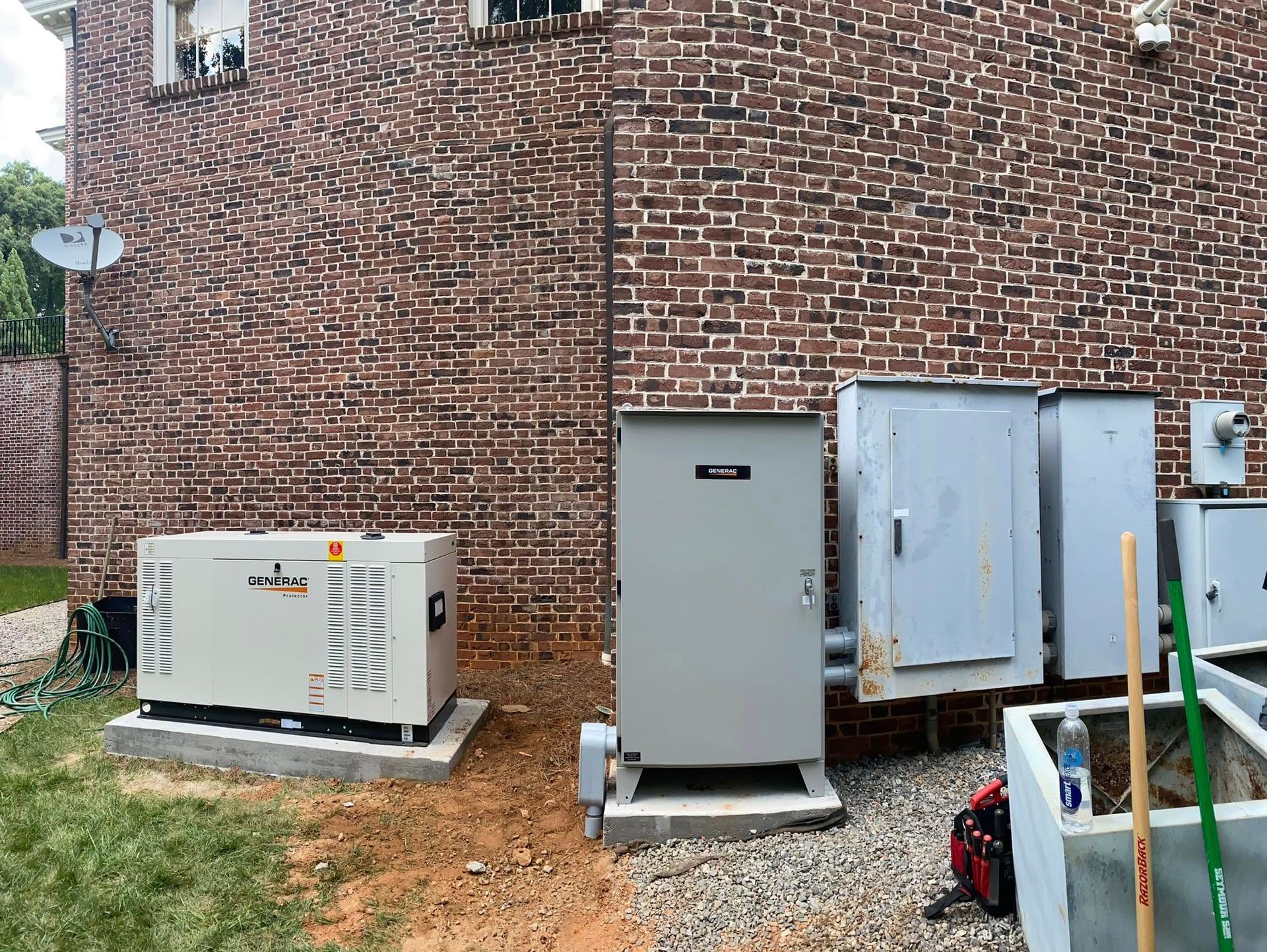 Outdoor HVAC units beside a brick building, with a gray cabinet and electrical boxes on concrete pads.