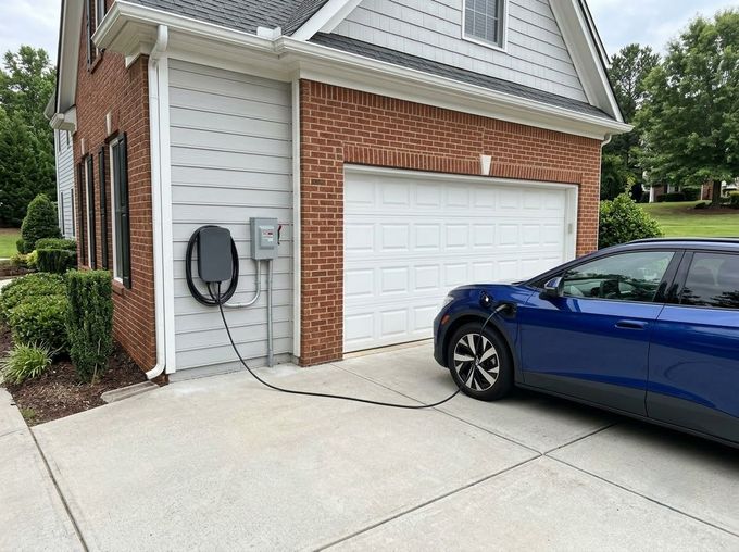 Blue car plugged into a charging station beside a brick-and-siding garage
