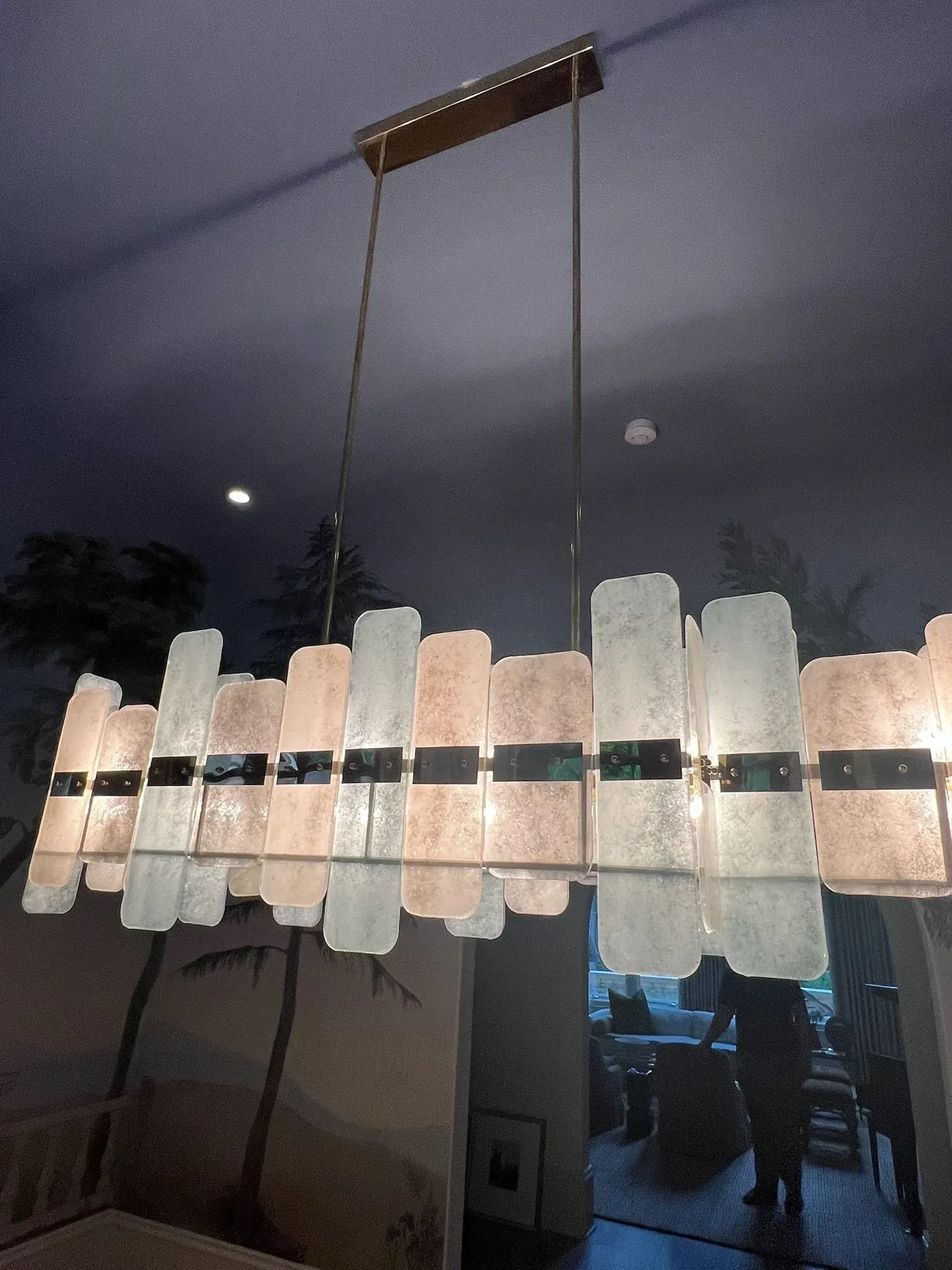 Hanging chime made of pale rectangular pieces and dark bars, suspended indoors against a dim evening sky.