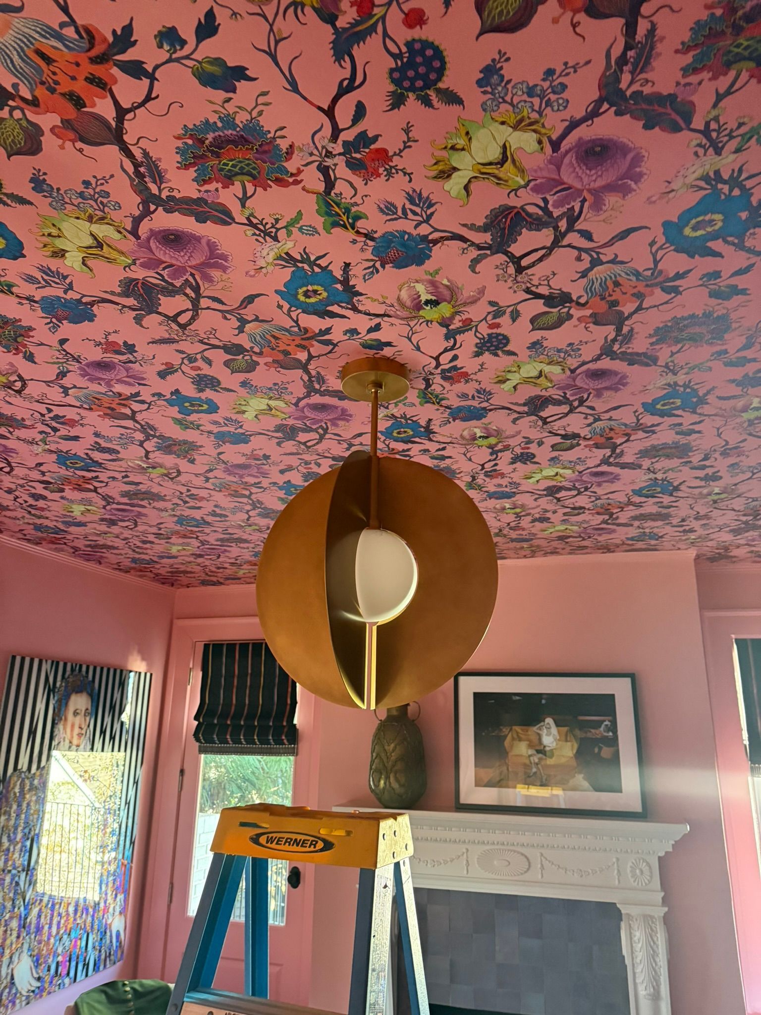 Colorful ceiling mural above a room with a ladder and a large gold hanging sculpture
